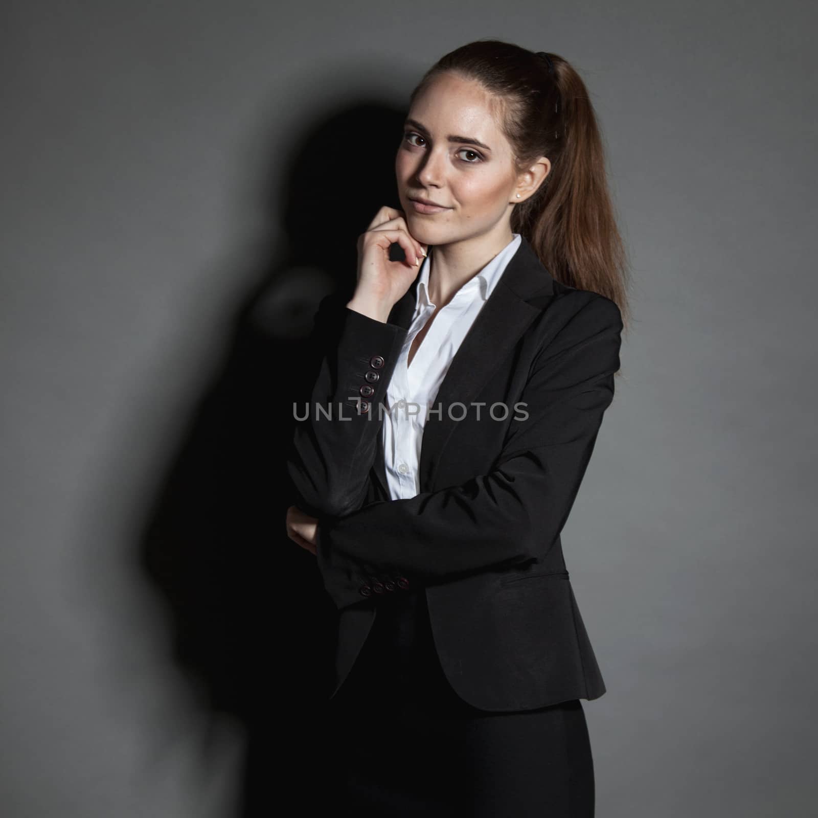 Portrait of young businesswoman in black suit on dark background