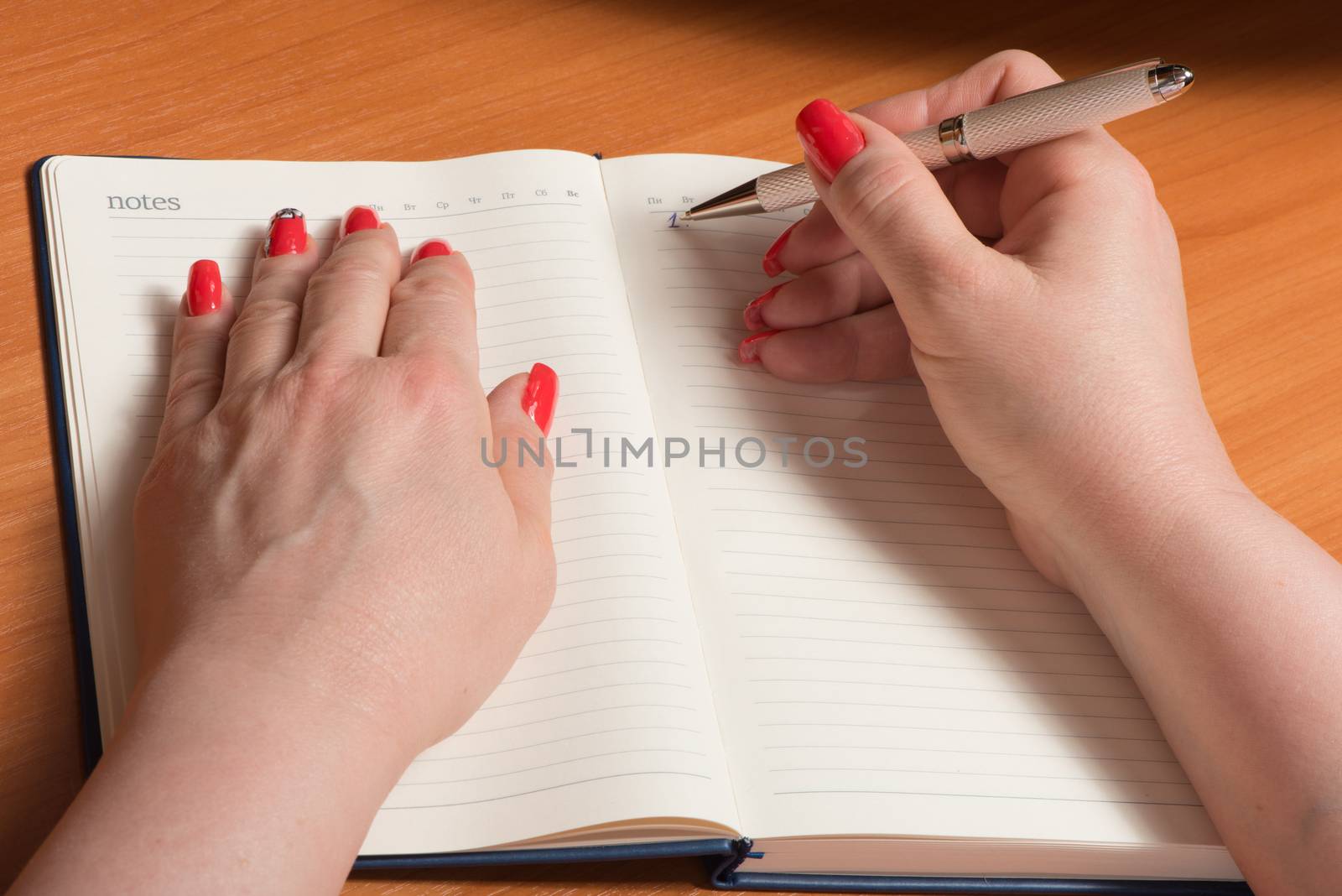 Female hands with manicure over pages of a notebook hold a pen