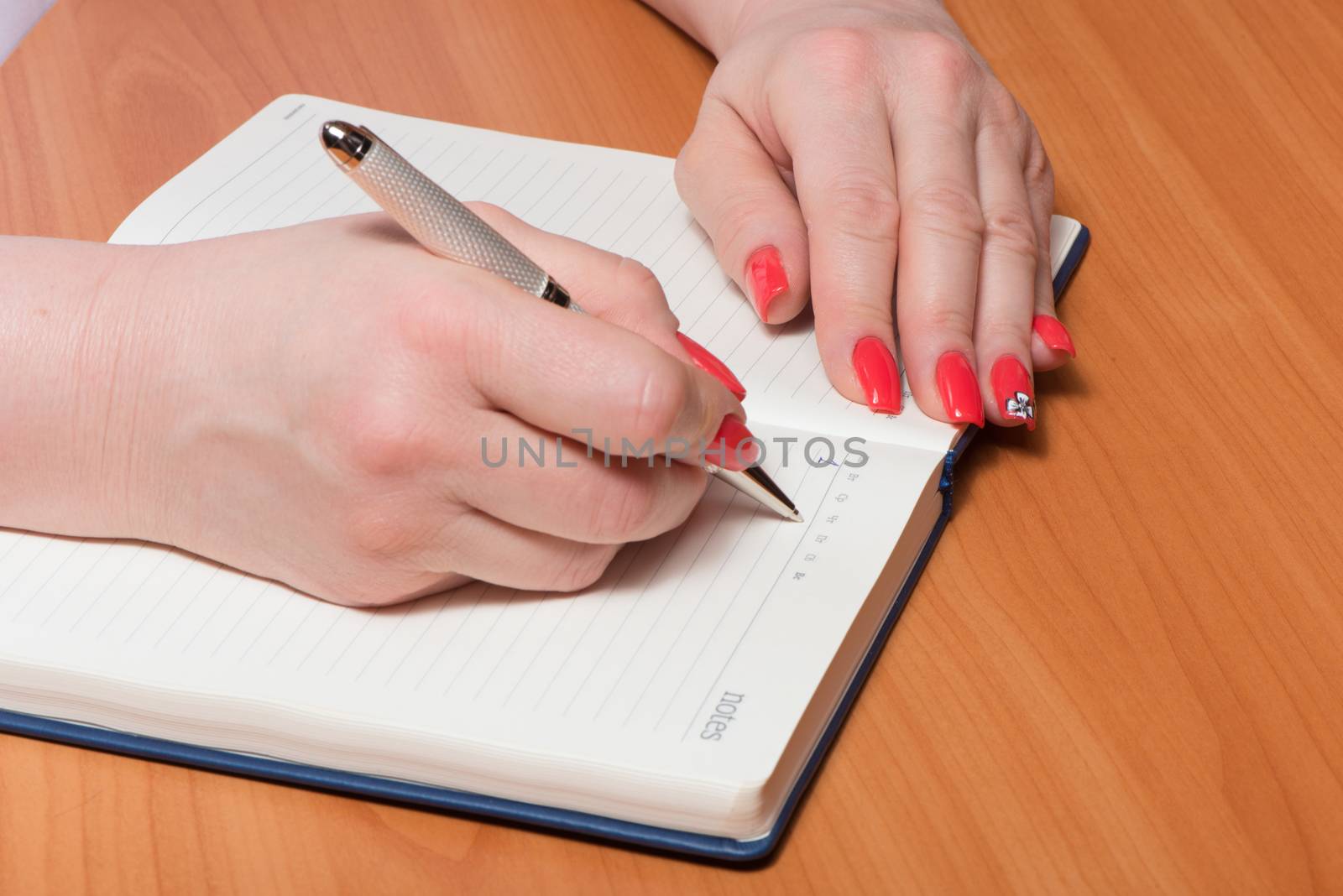 Female hands with manicure over pages of a notebook hold a pen