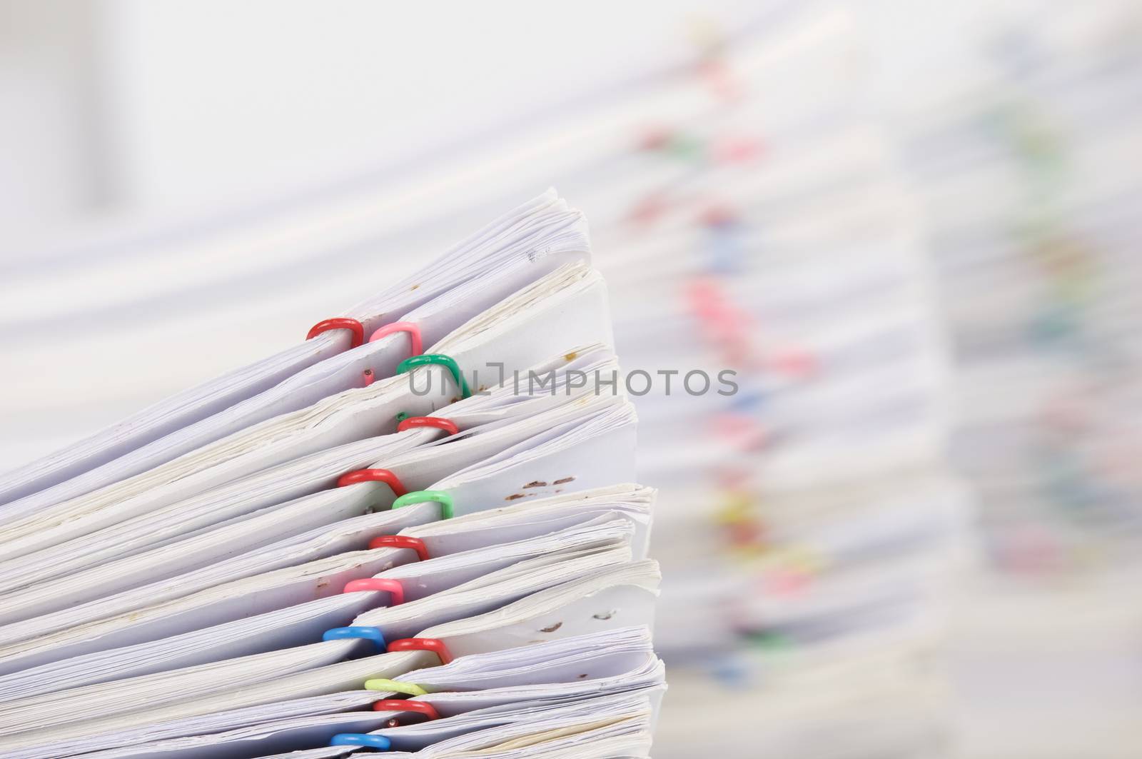 Pile overload paperwork of report with colorful paperclip have blur pile overload document as background place on white table.