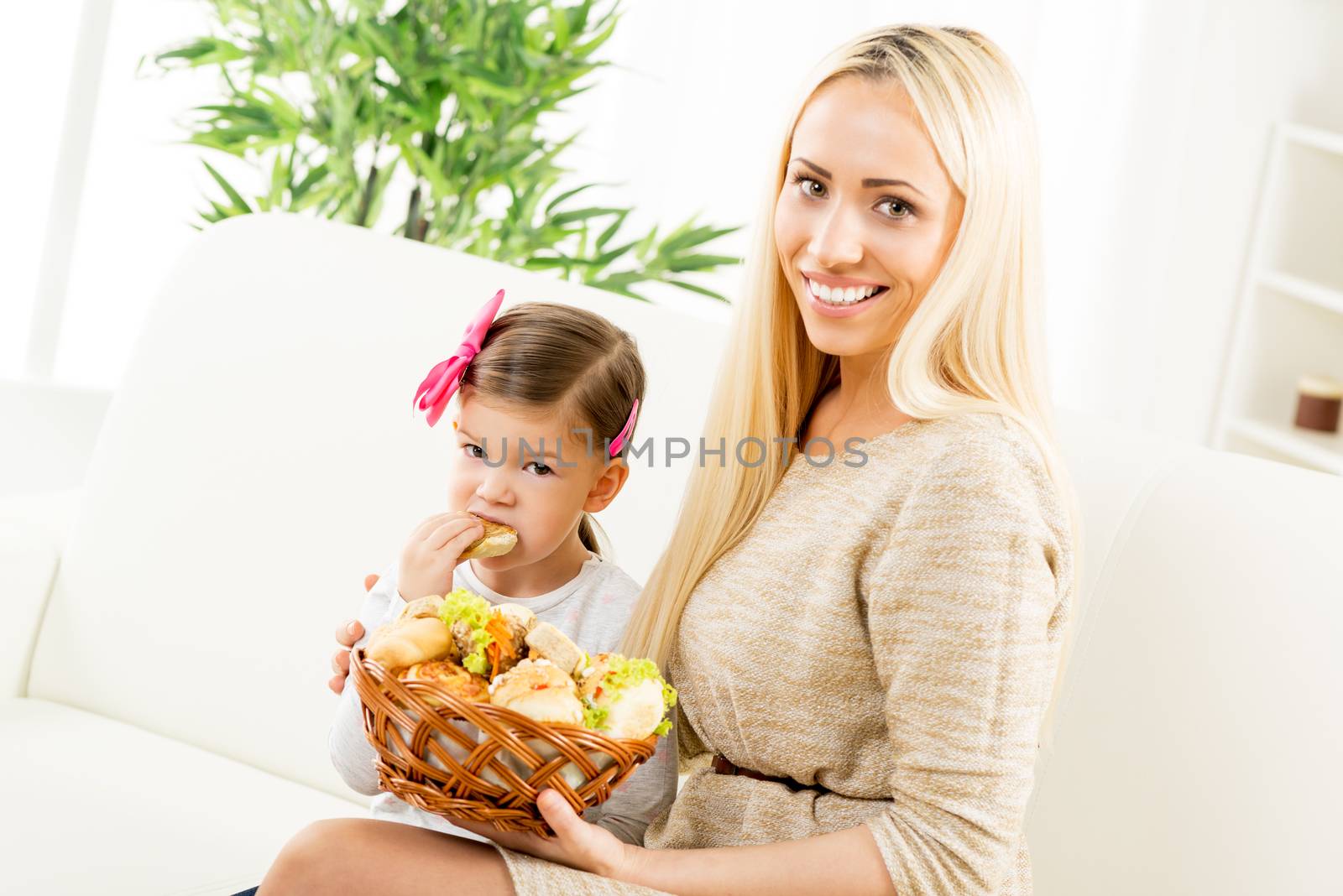 A beautiful young mother gives a wicker basket with fresh pastries her daughter by offering her a variety of delicious baked goods. With a smile looking at the camera.