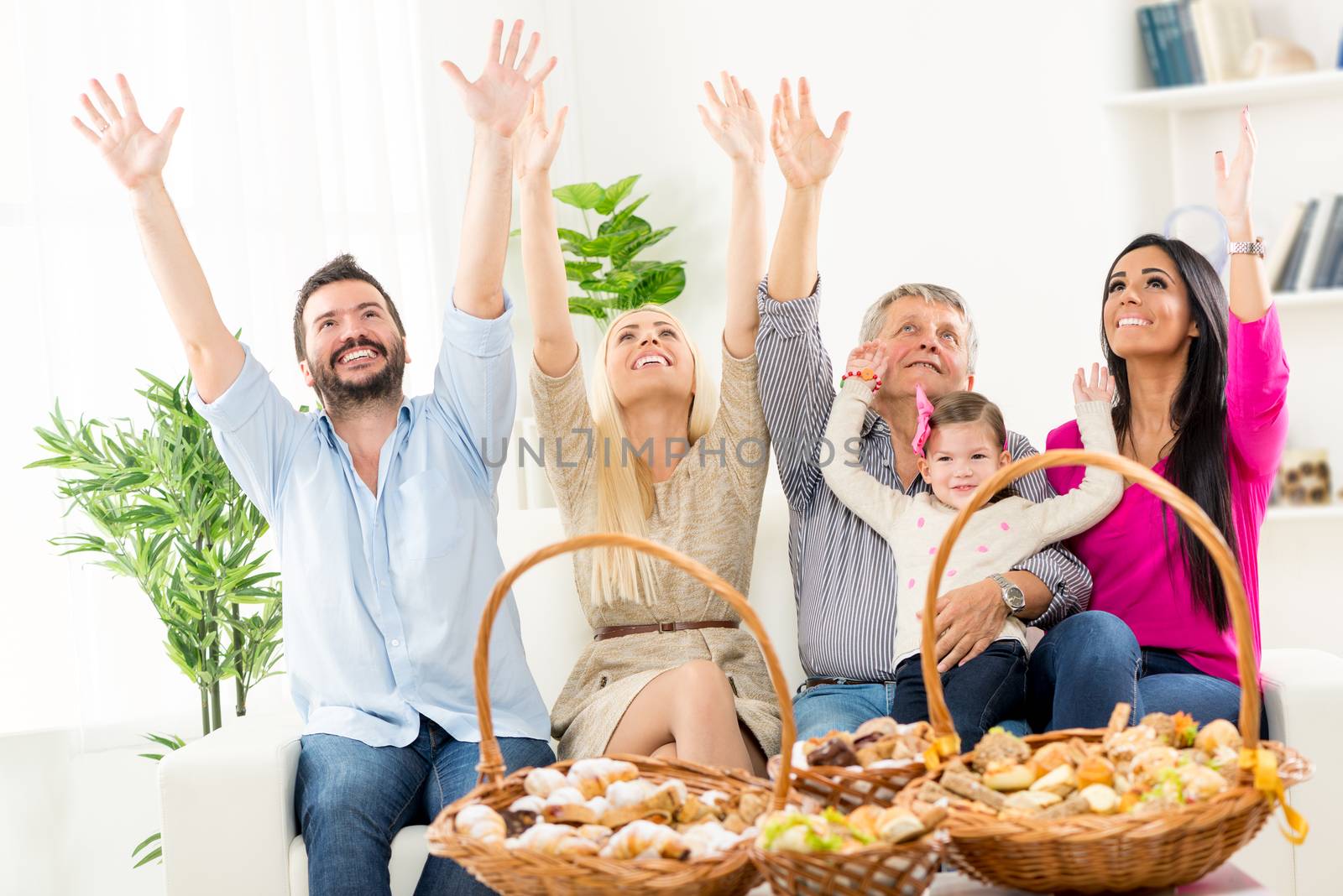 Happy family sitting on couch with arms raised, looking up. In front of them on the table are woven baskets decorated with beautiful pastries.