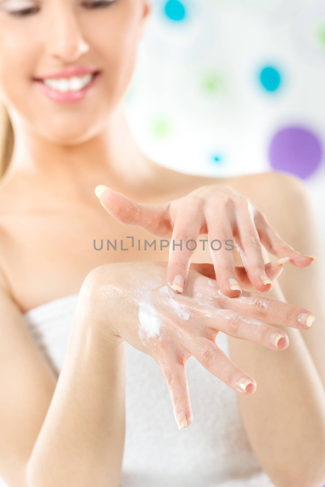 The young beautiful girl with a towel wrapped around her chest applied the cream on her hands. The focus is on the hands.