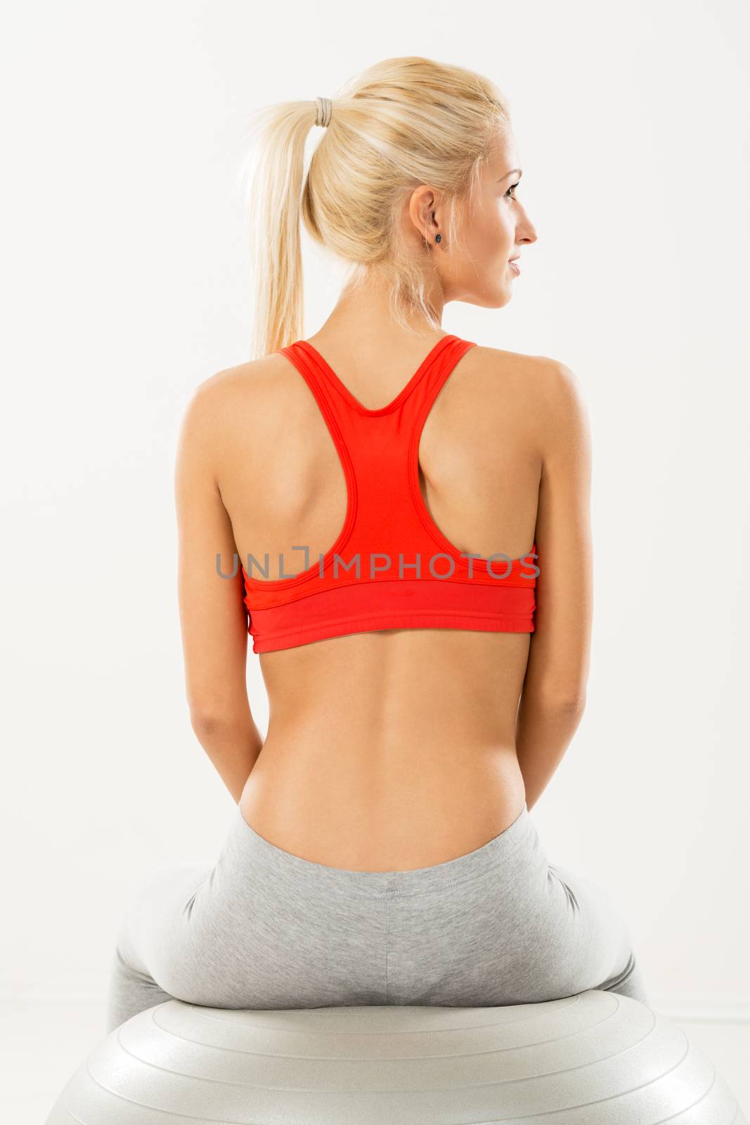 Cute sporty Young girl sitting to pilates ball and resting. Rear view.