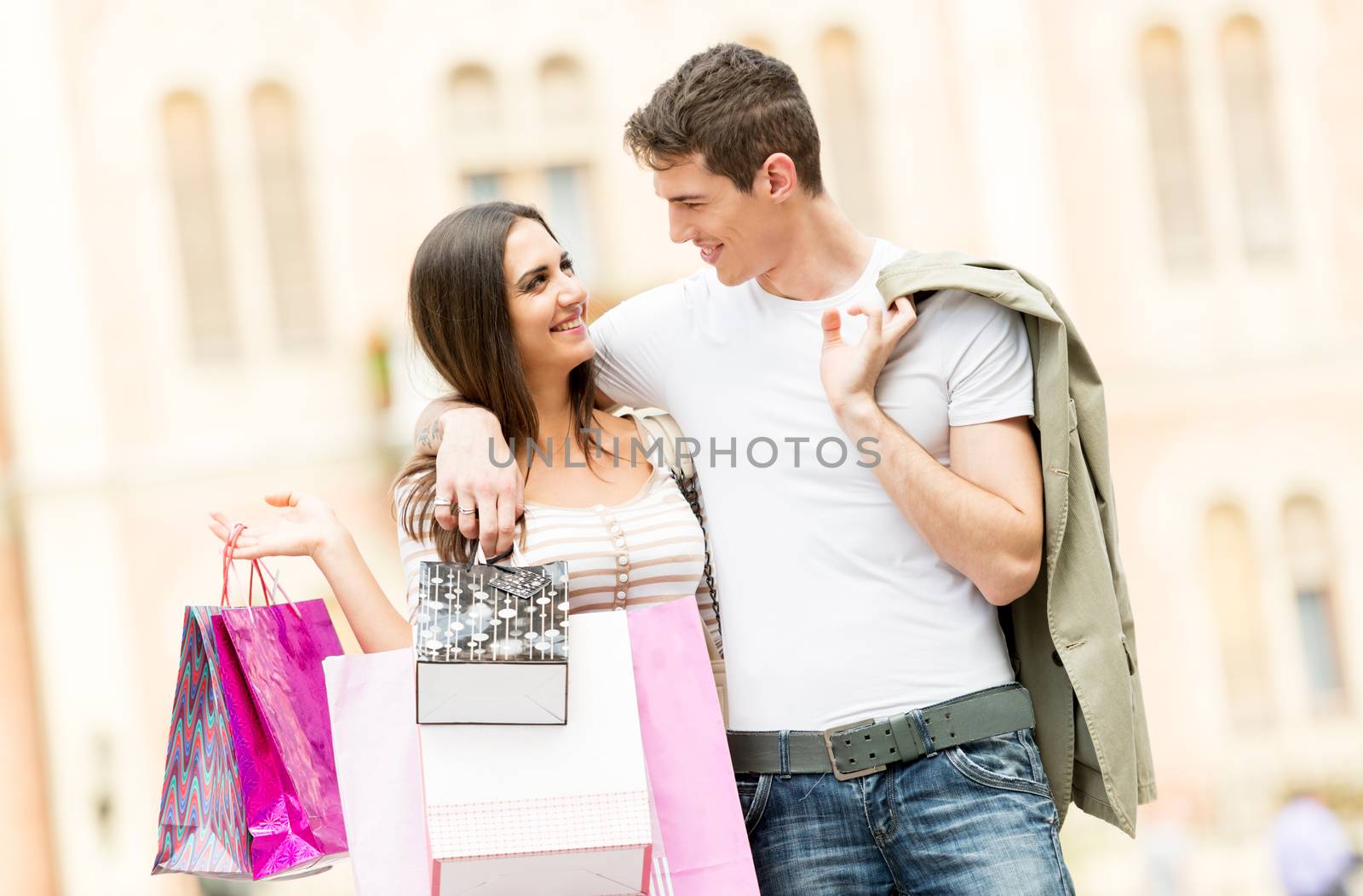 Young happy heterosexual smiling couple walking, carrying in his hands a bunch of shopping bags.