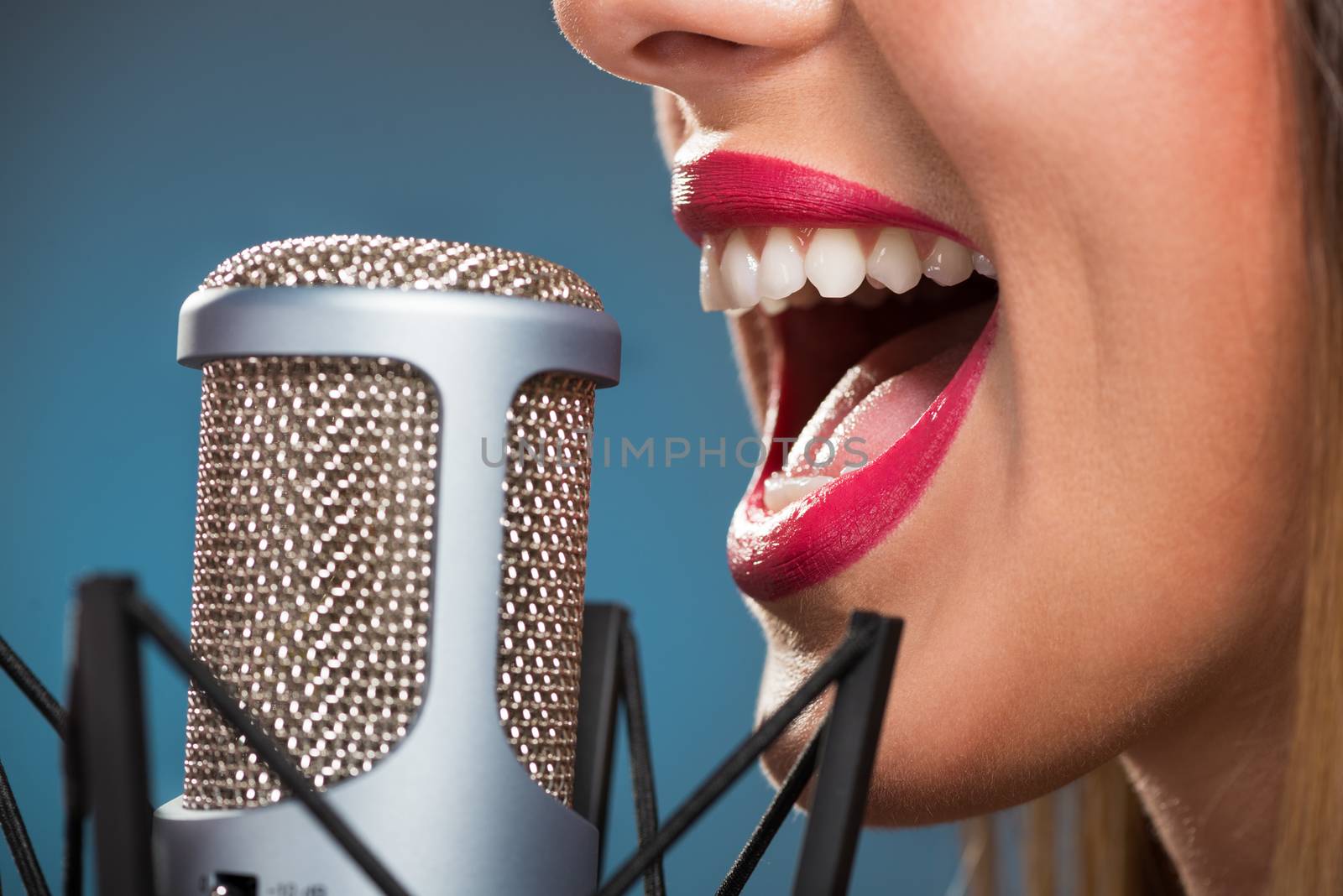 Close-up of female open mouth with red lipstick in front of microphone.