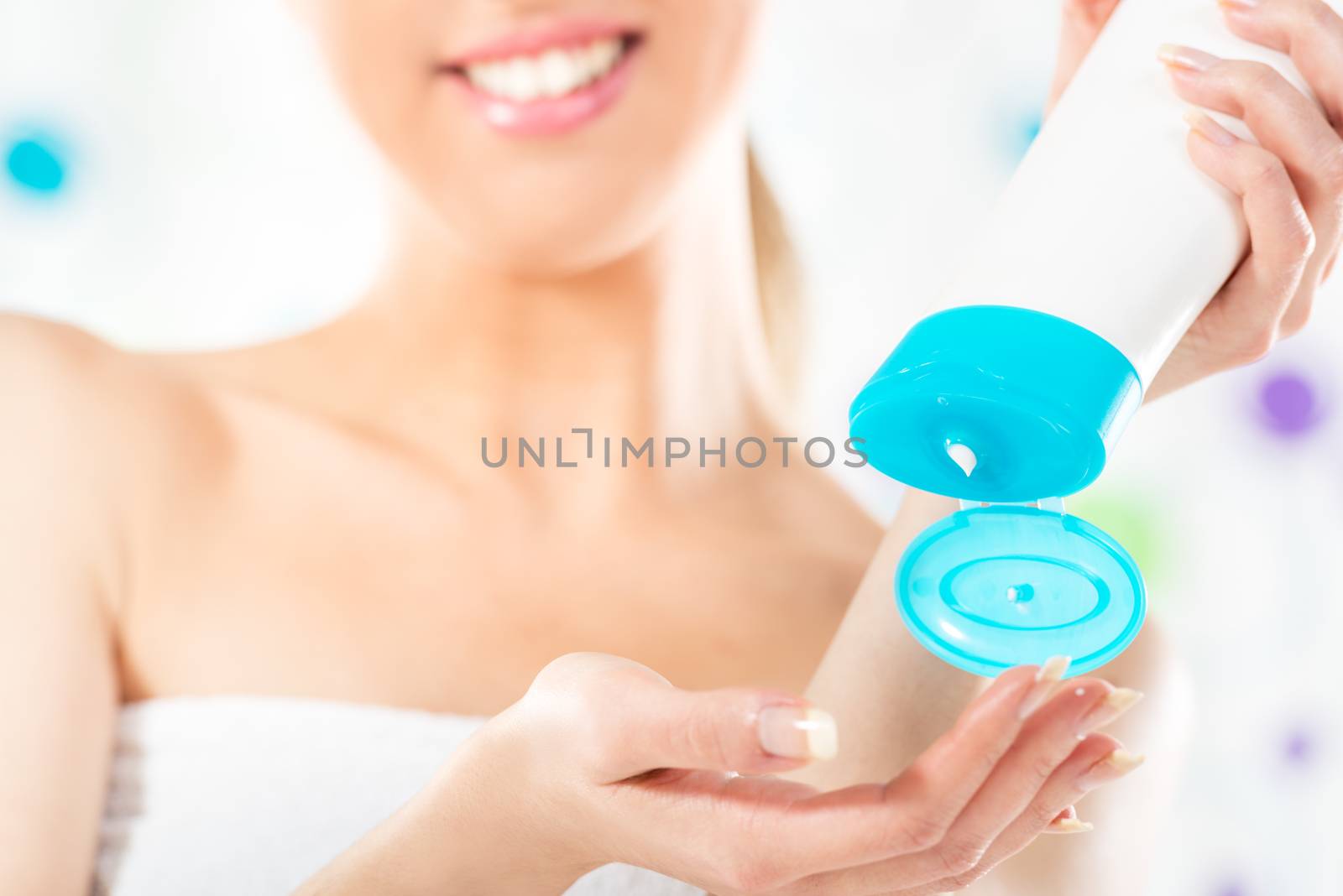 Close-up tube of cosmetic products in the hands of a young woman, unrecognizable face with a towel wrapped around her chest.