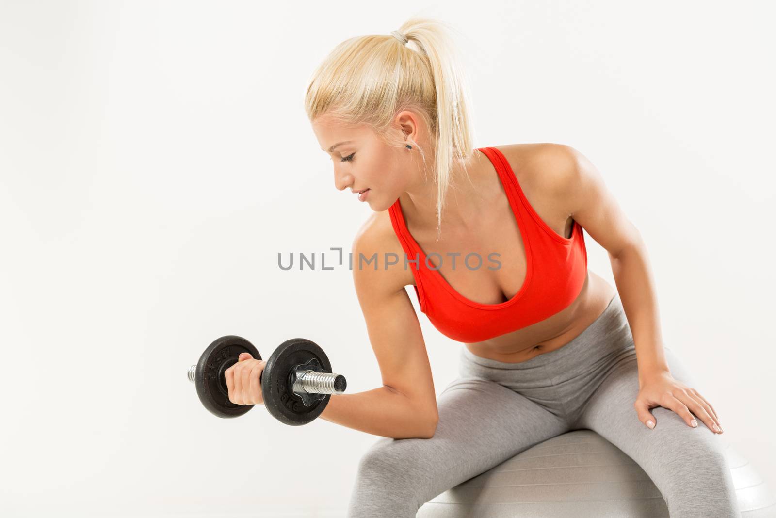 Cute sporty Young girl sitting to pilates ball and exercising with dumbbells.
