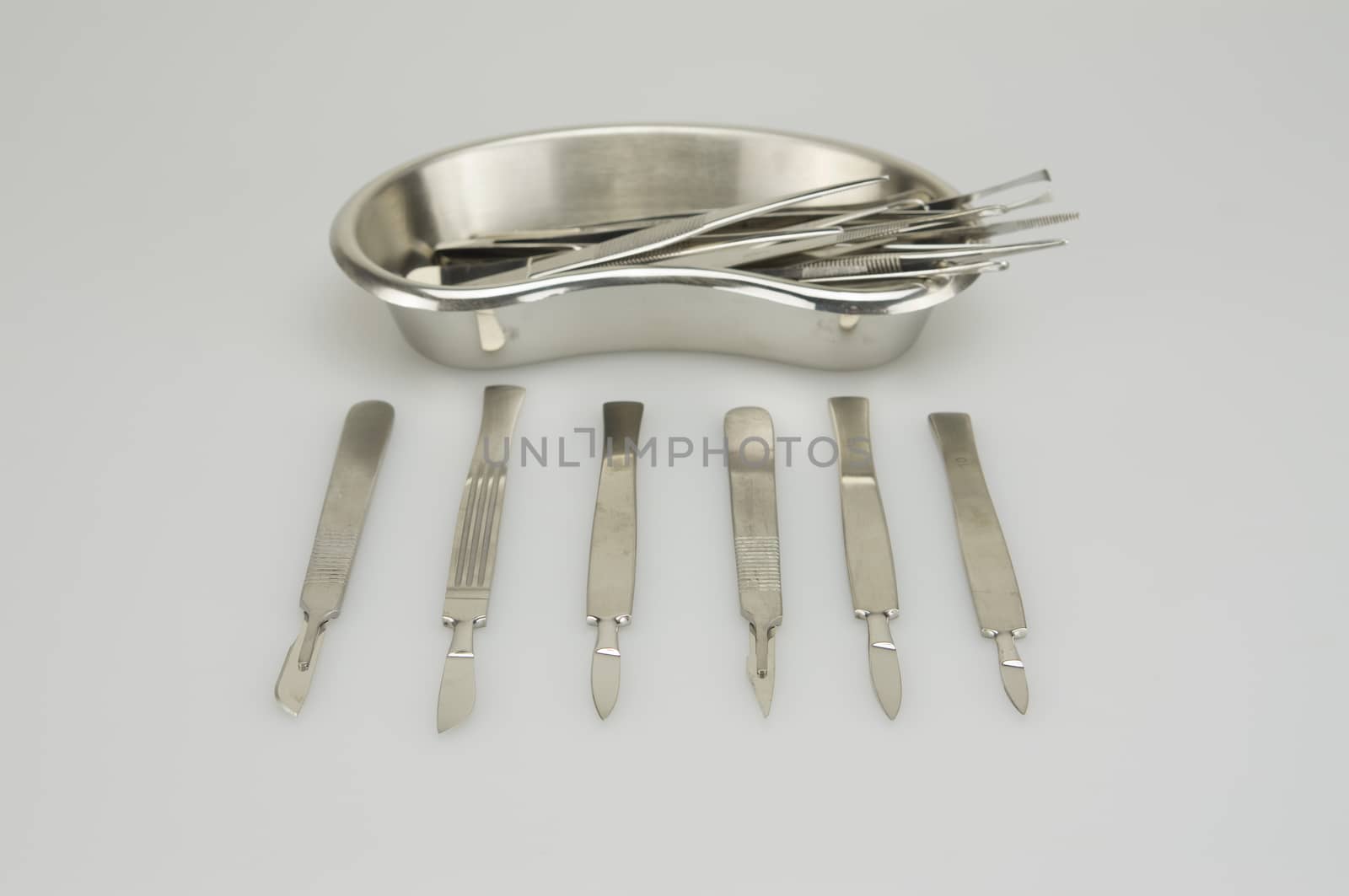 Many types of forceps and scalpel in kidney shape bowl on white background.