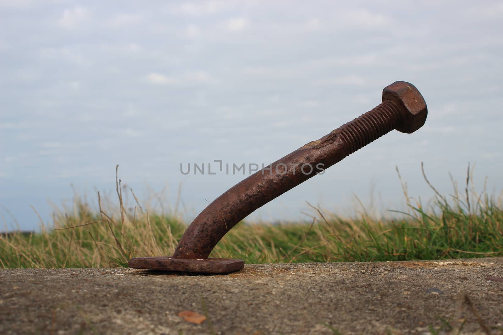 Bended rusty bolt in concrete with clouds