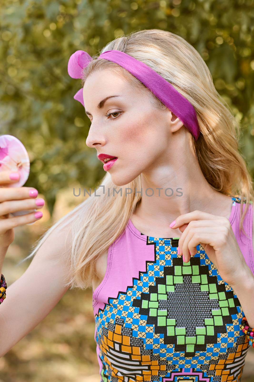 Beauty portrait stylish playful woman primping with mirror in park, people, outdoors. Attractive hipster happy pretty blonde girl with bow, fashionable top. Relax in summer garden, lifestyle, bokeh