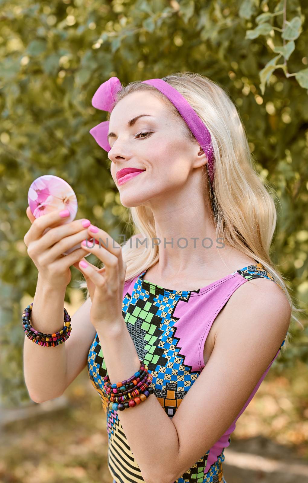 Beauty portrait stylish playful woman smiling primping with mirror, park, people, outdoors. Attractive hipster happy pretty blonde girl with bow, fashionable top. Relax, summer garden, lifestyle,bokeh