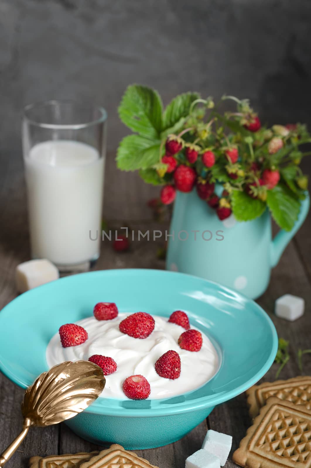 Strawberry with cream in a ceramic Cup, cookies and milk in glass on old wooden surface. Bouquet with strawberries in a ceramic vase and antique spoon In a rustic style.