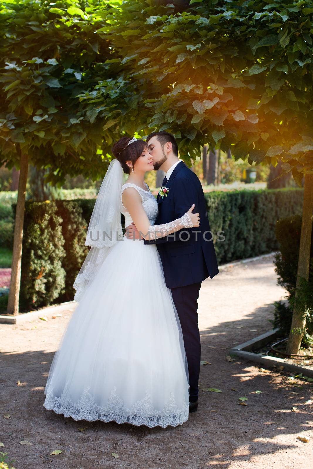 Happy smiling newlyweds walking outdoors, kissing and embracing on their wedding day