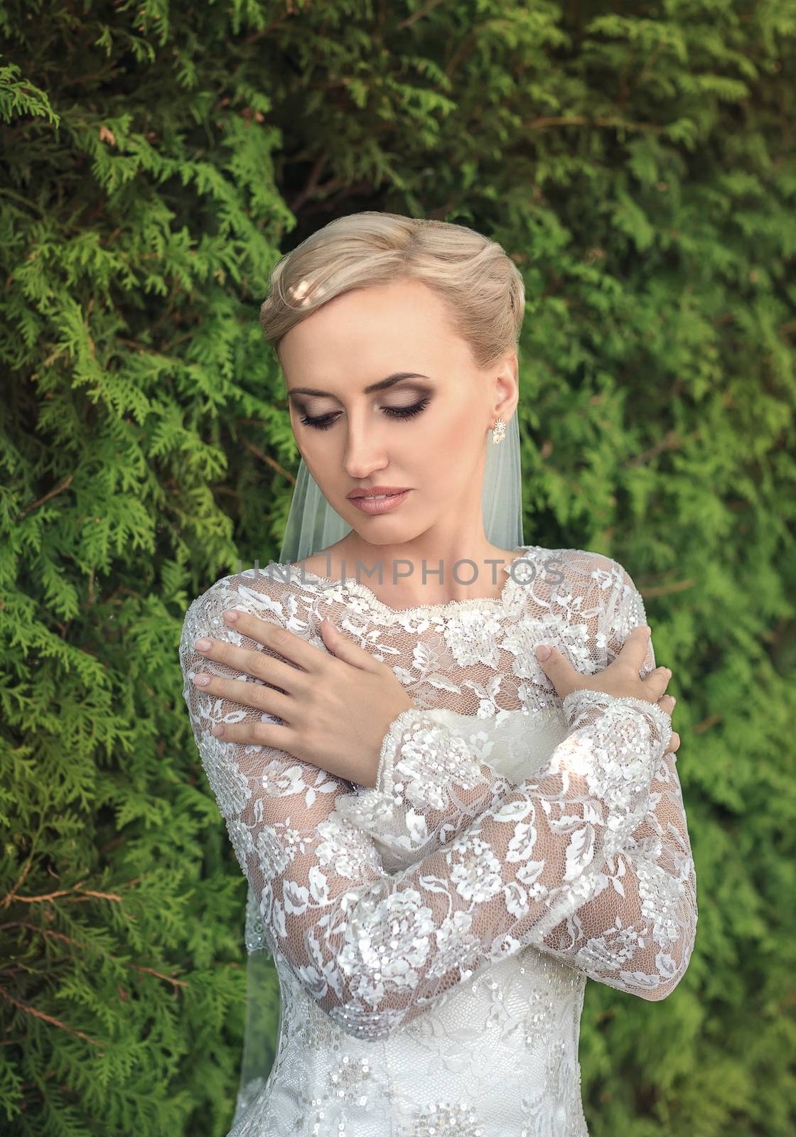 Beauty bride in bridal gown with bouquet and lace veil on the nature. Beautiful model girl in a white wedding dress. Female portrait in the park. Woman with hairstyle. Cute lady outdoors