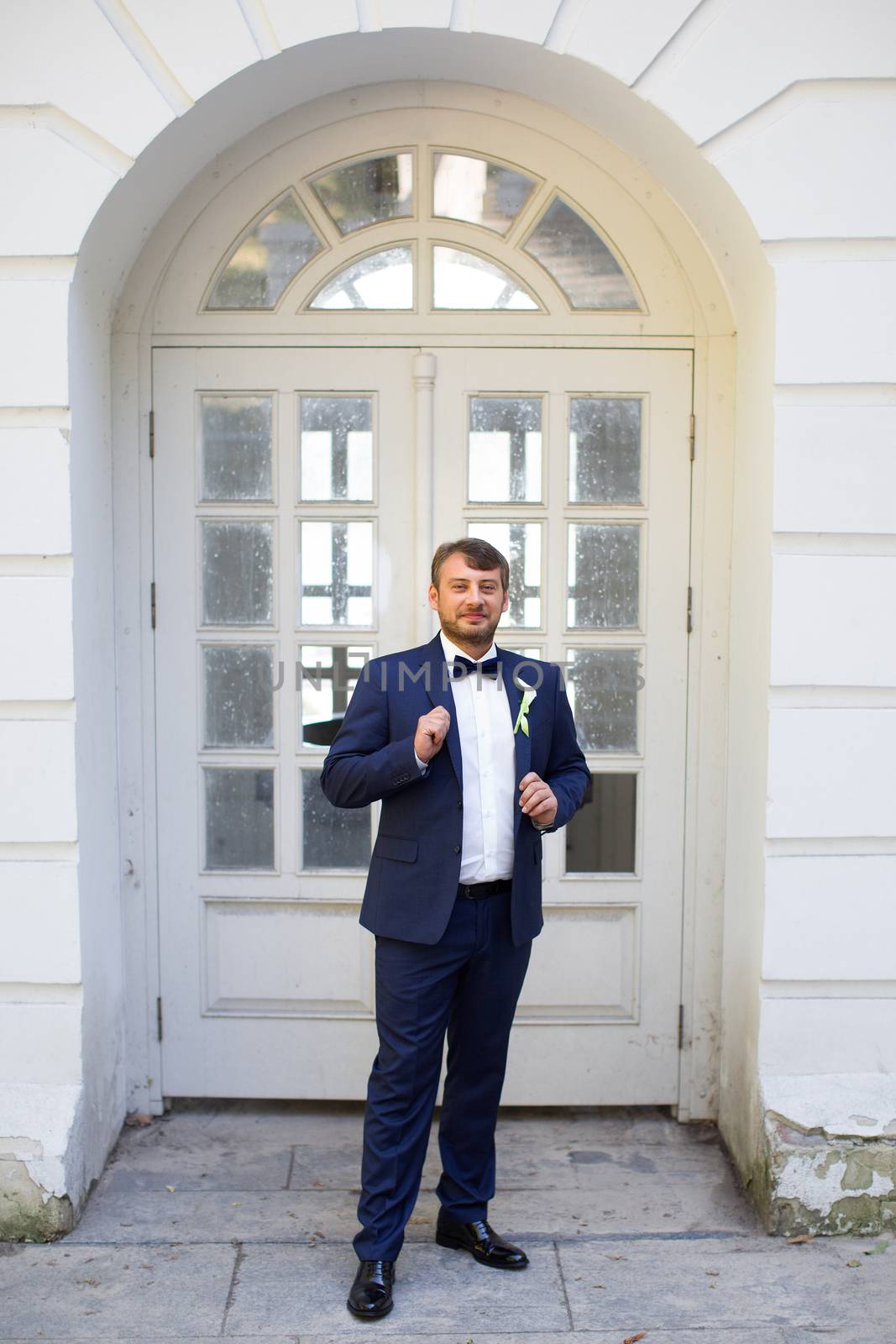 Happy handsome smiling groom in black suit with boutonniere