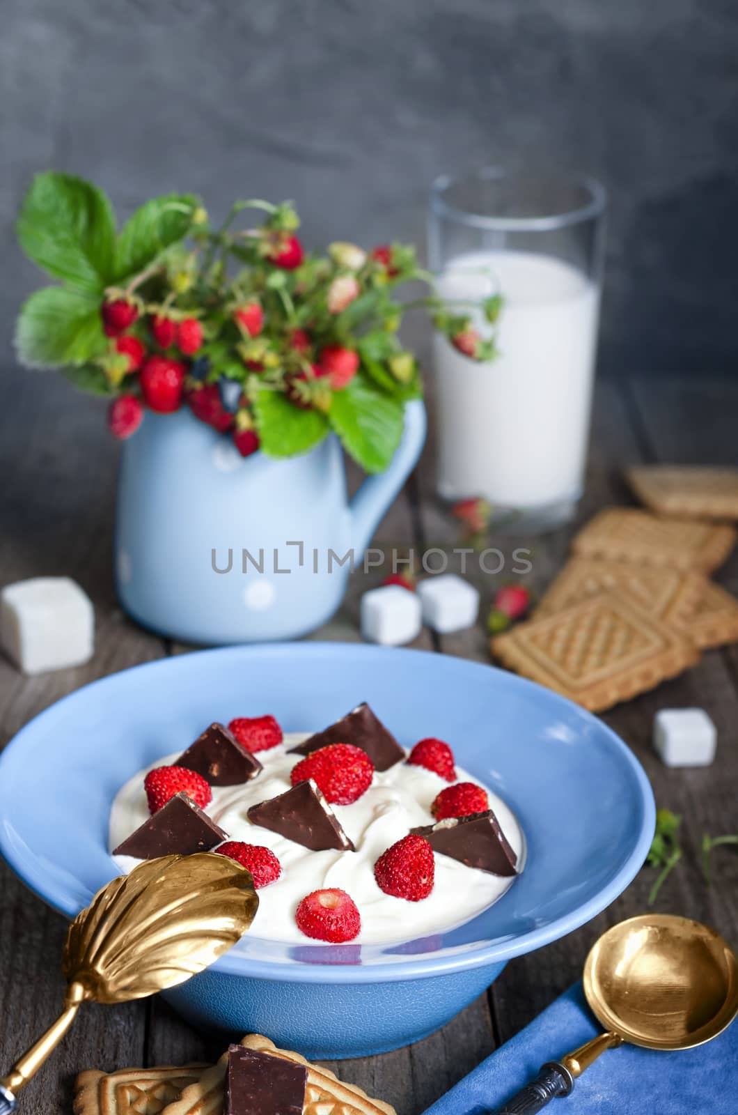 Strawberry with cream in a bowl, cookies and milk in glass on old wooden surface. Bouquet with strawberries in a vase and antique spoon in a rustic style.