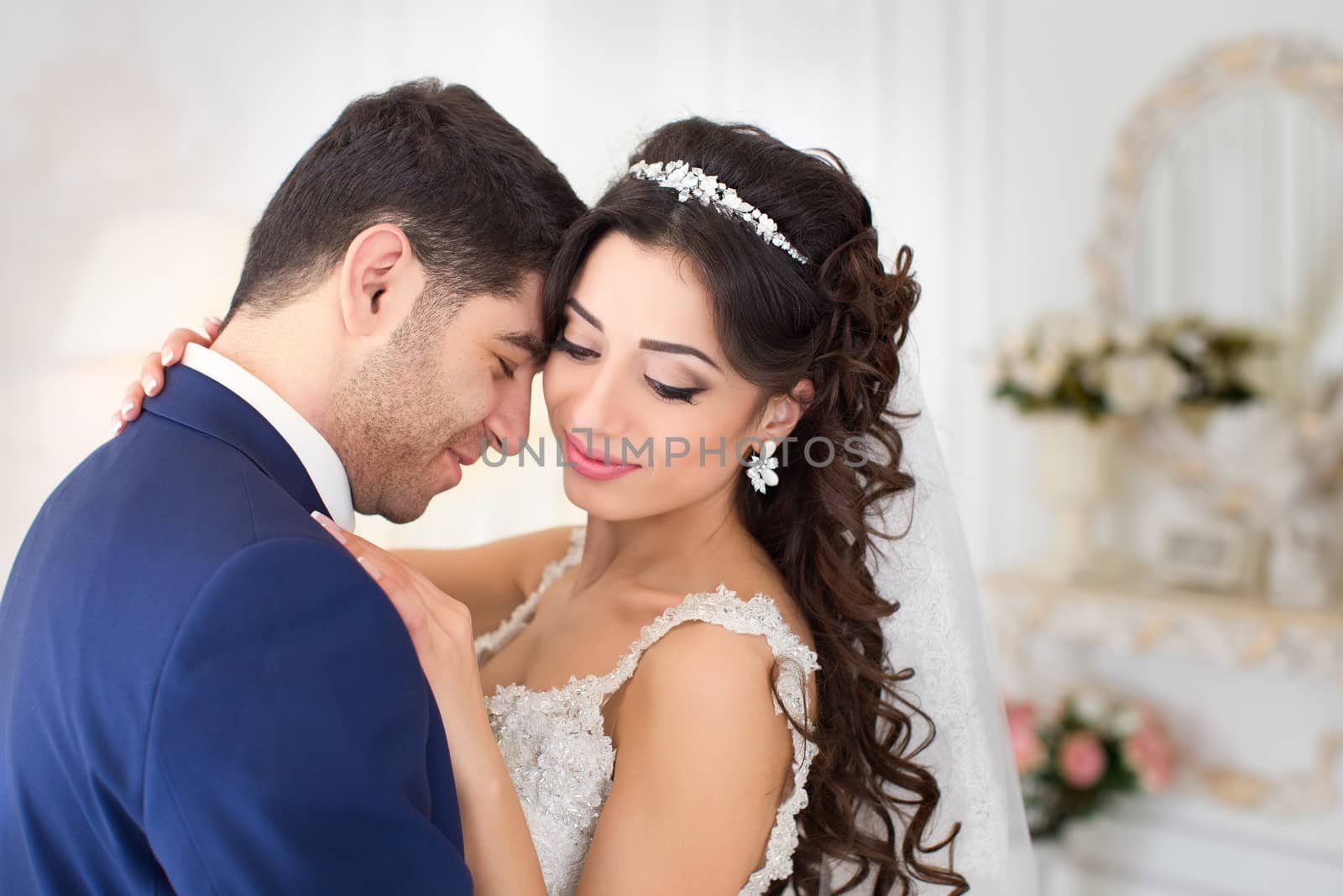 Studio portrait of young elegant enamored just married bride and groom and  embracing on grey background