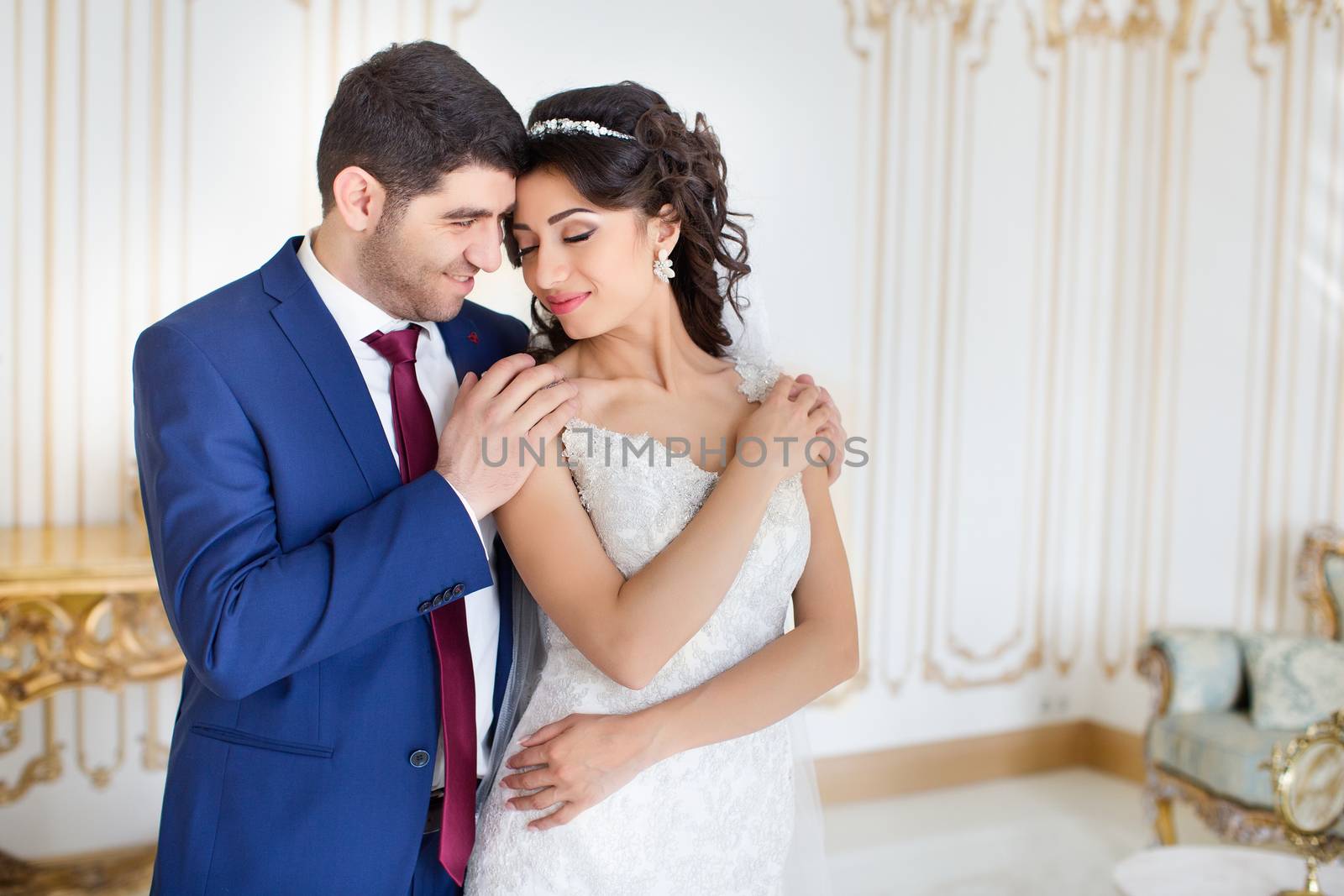 Studio portrait of young elegant enamored just married bride and groom and  embracing on grey background