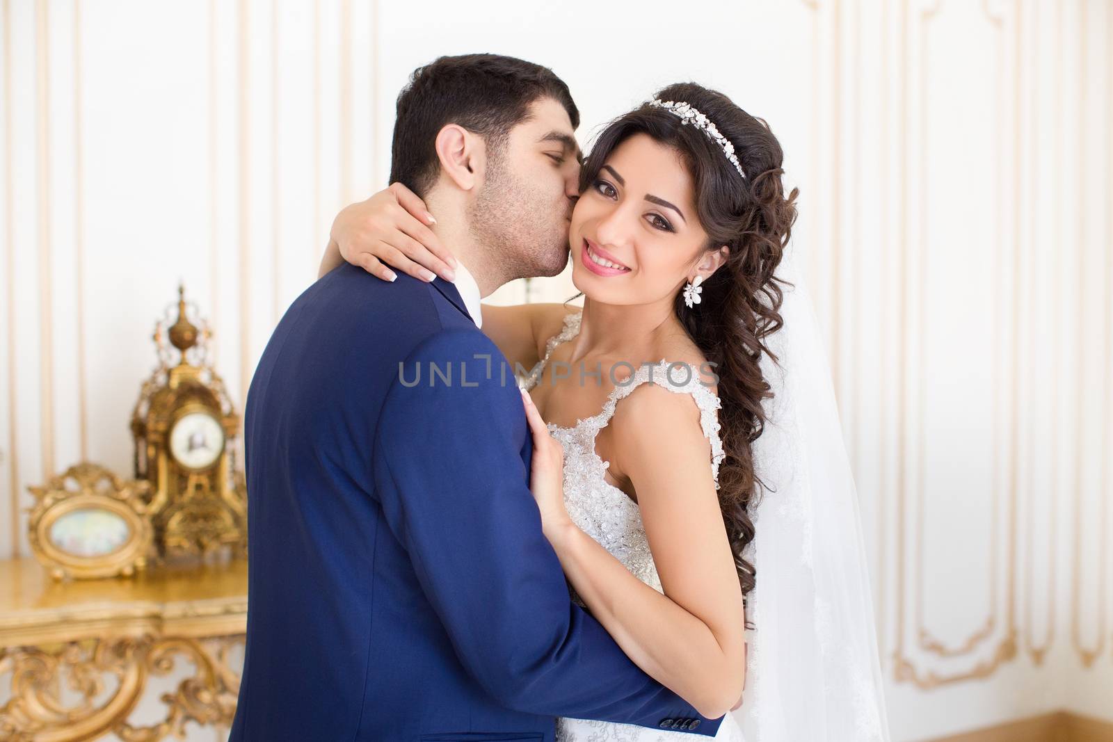 Studio portrait of young elegant enamored just married bride and groom and  embracing on grey background