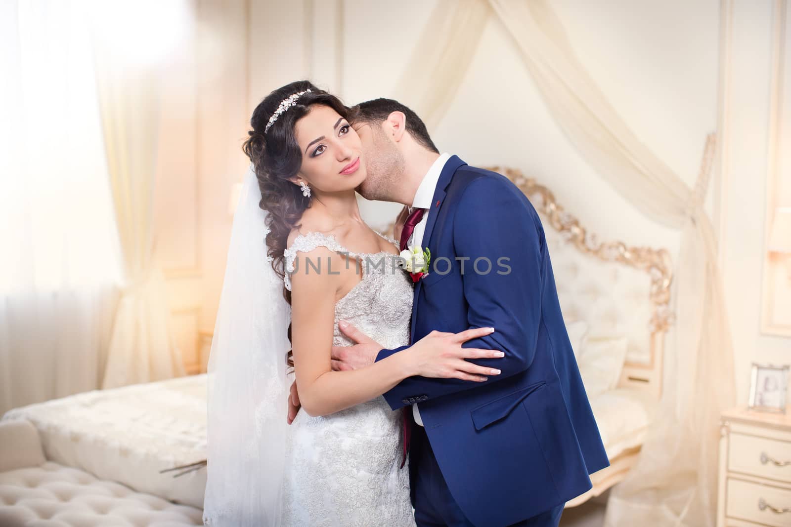 Studio portrait of young elegant enamored just married bride and groom and  embracing on grey background