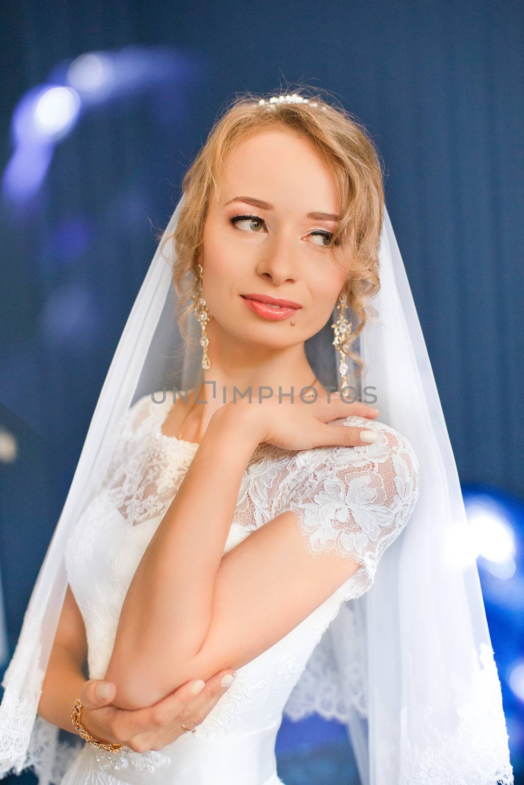 Portrait of beautiful bride with fashion veil posing on bed at wedding morning. Makeup. Brunette girl with long wavy hair styling. Wedding dress.