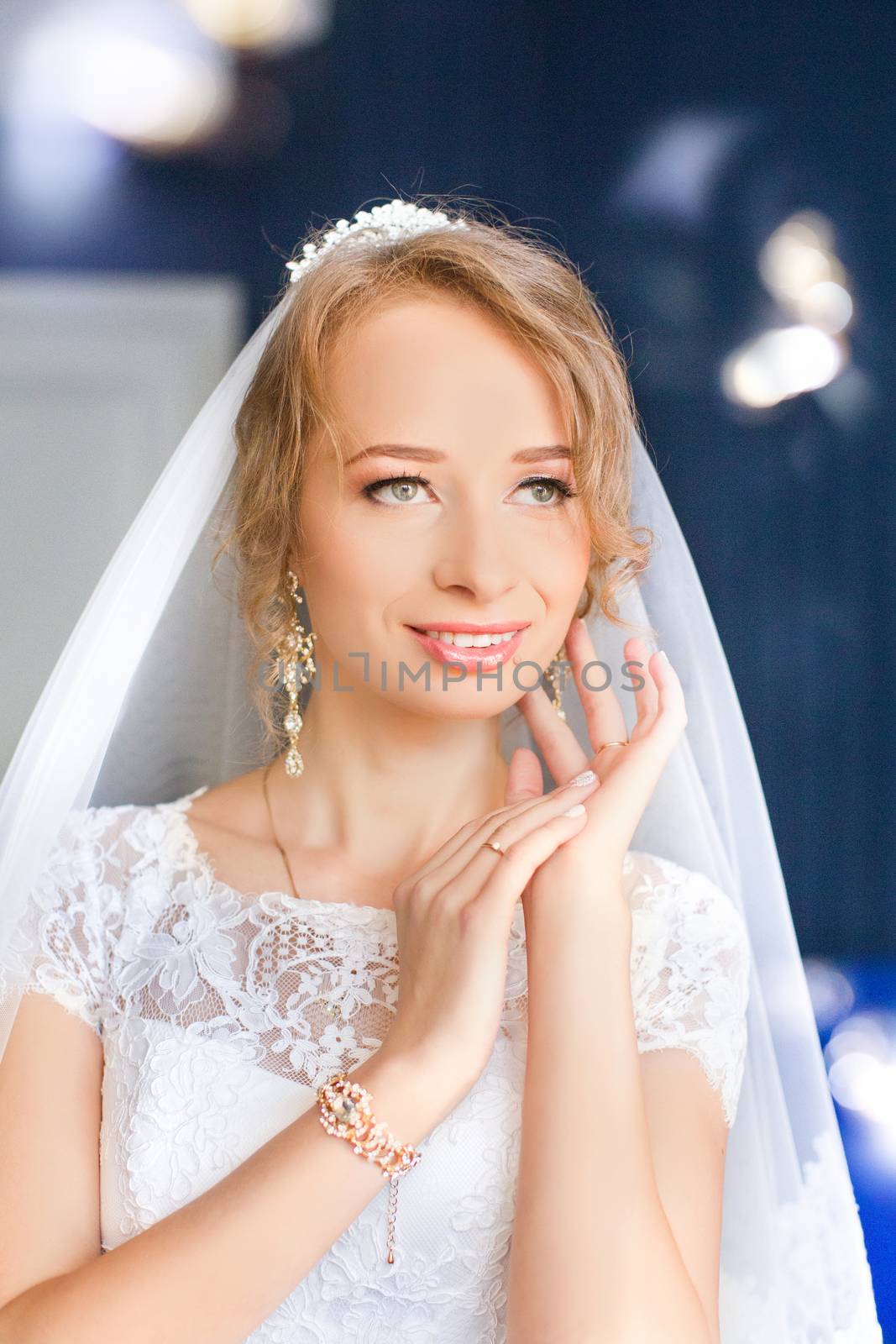 Portrait of beautiful bride with fashion veil posing on bed at wedding morning. Makeup. Brunette girl with long wavy hair styling. Wedding dress.