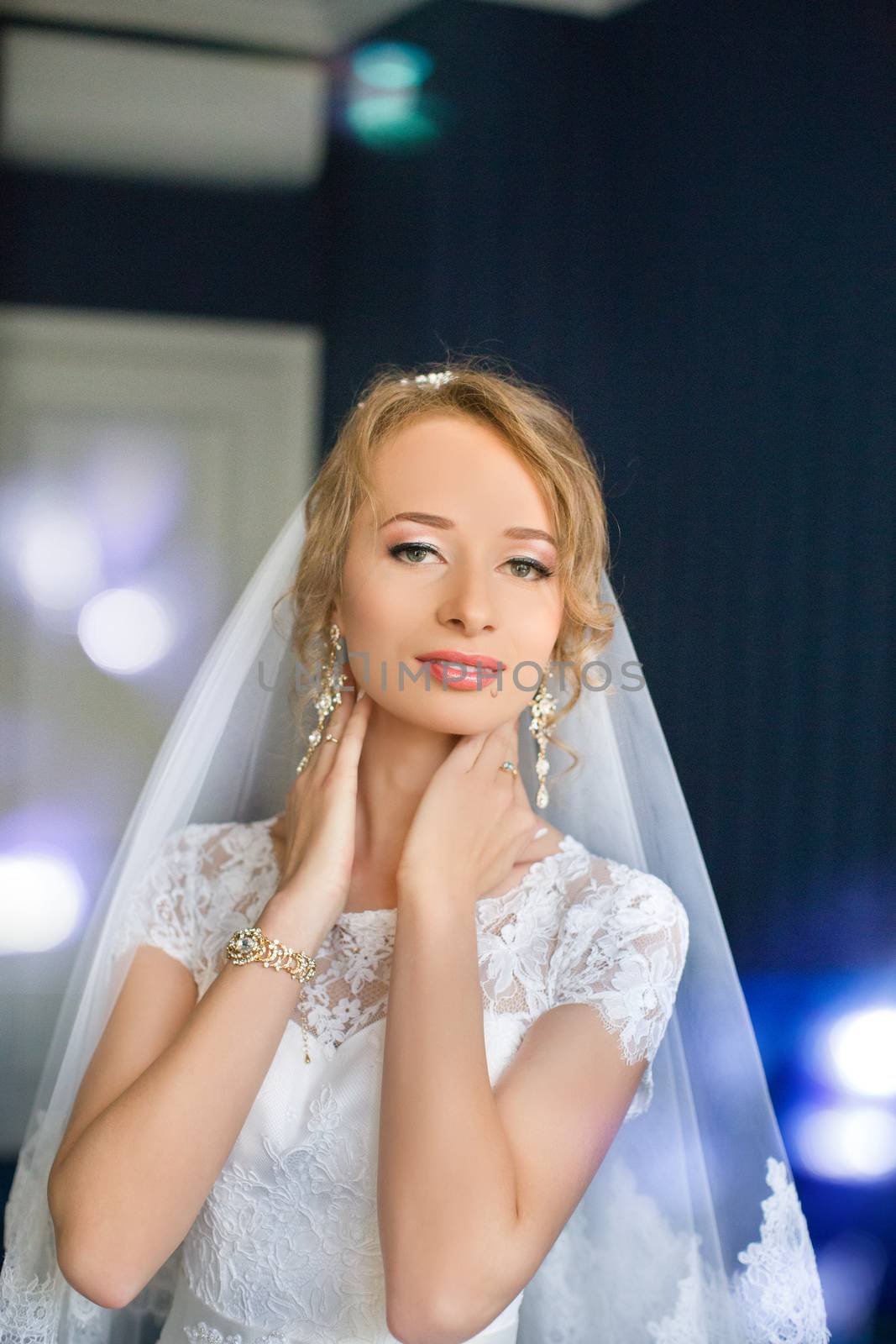 Portrait of beautiful bride with fashion veil posing on bed at wedding morning. Makeup. Brunette girl with long wavy hair styling. Wedding dress.