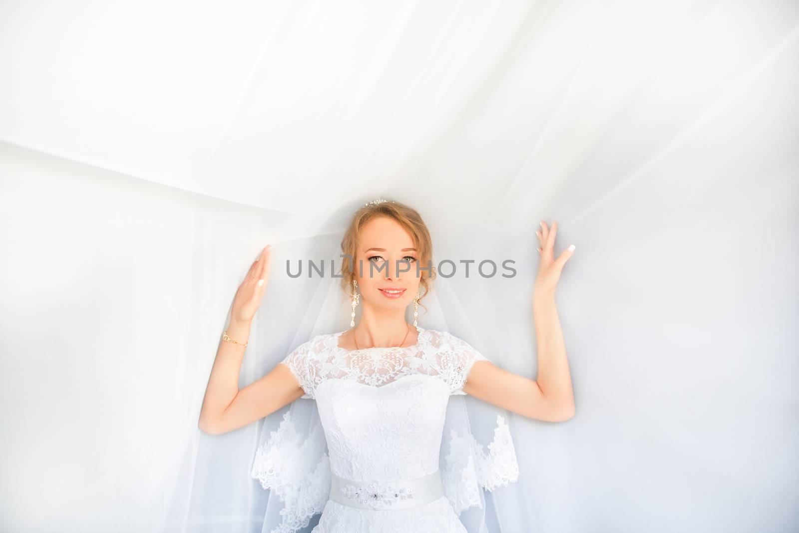 Portrait of beautiful bride with fashion veil posing on bed at wedding morning. Makeup. Brunette girl with long wavy hair styling. Wedding dress.