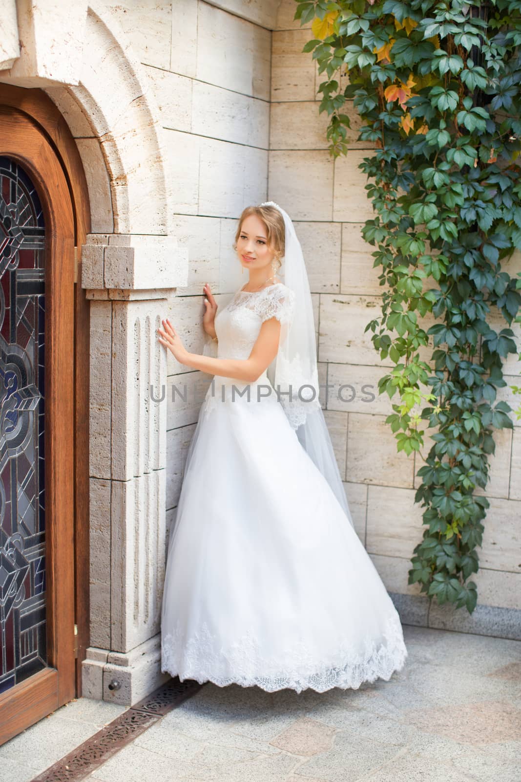 Portrait of beautiful bride with fashion veil posing on bed at wedding morning. Makeup. Brunette girl with long wavy hair styling. Wedding dress. by lanser314