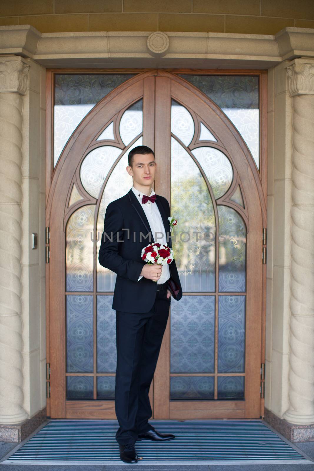 The groom holds a tie and smiles.Portrait of the groom in the park on their wedding day.