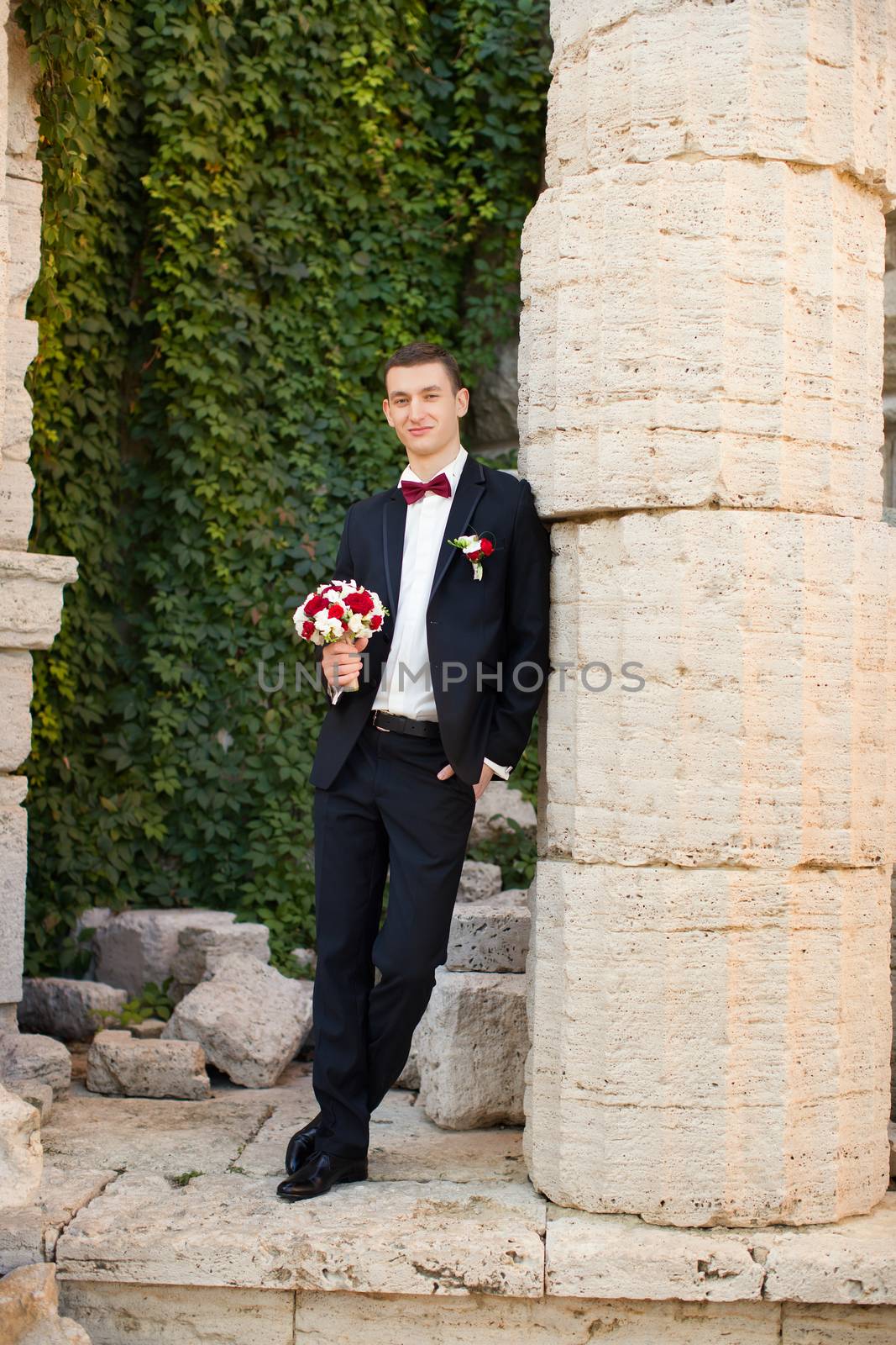 The groom holds a tie and smiles.Portrait of the groom in the park on their wedding day.