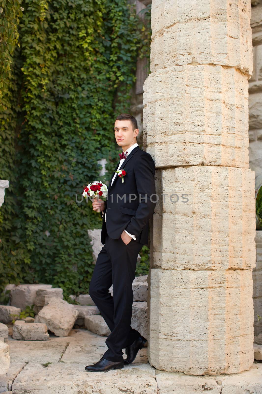 The groom holds a tie and smiles.Portrait of the groom in the park on their wedding day.