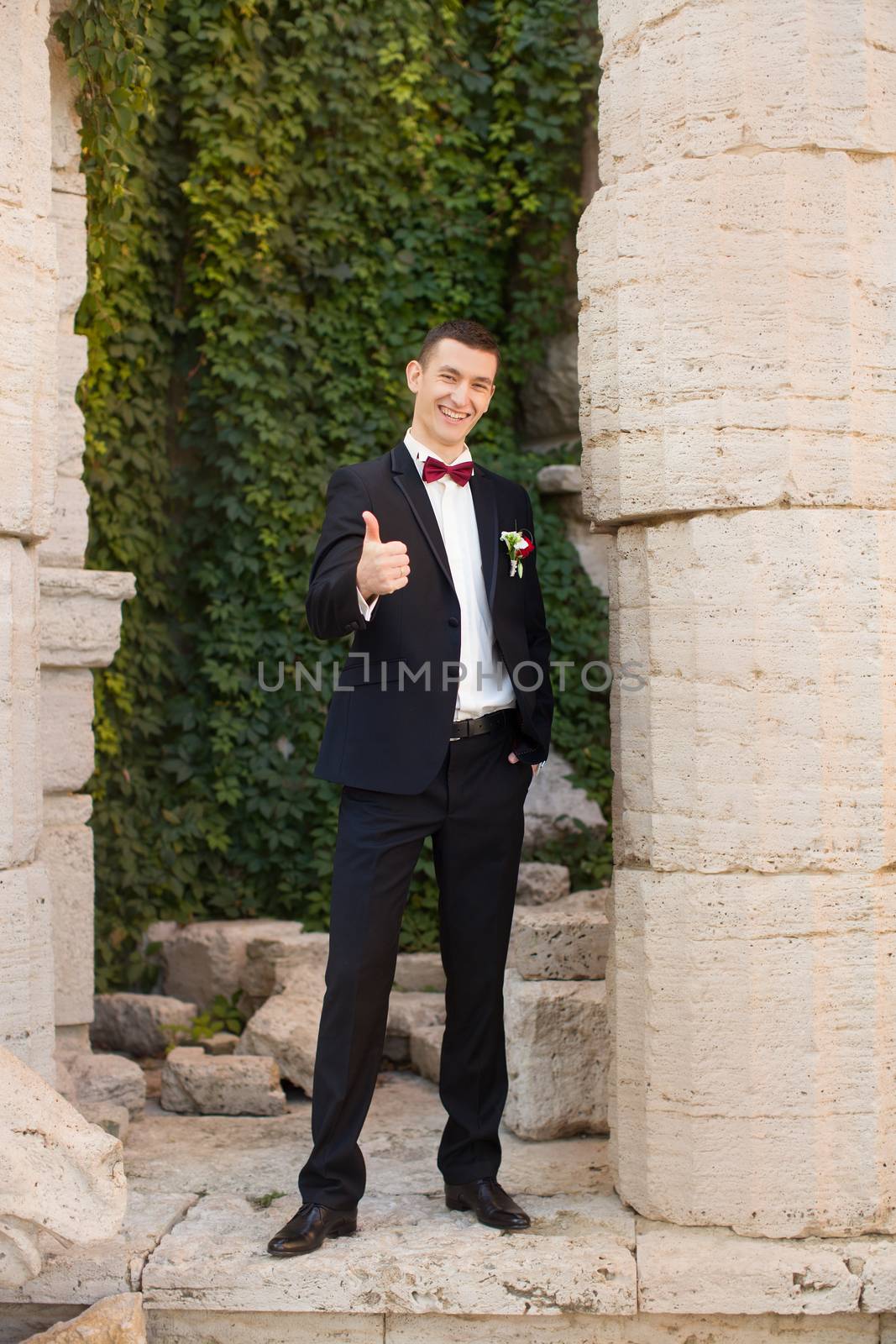 The groom holds a tie and smiles.Portrait of the groom in the park on their wedding day.