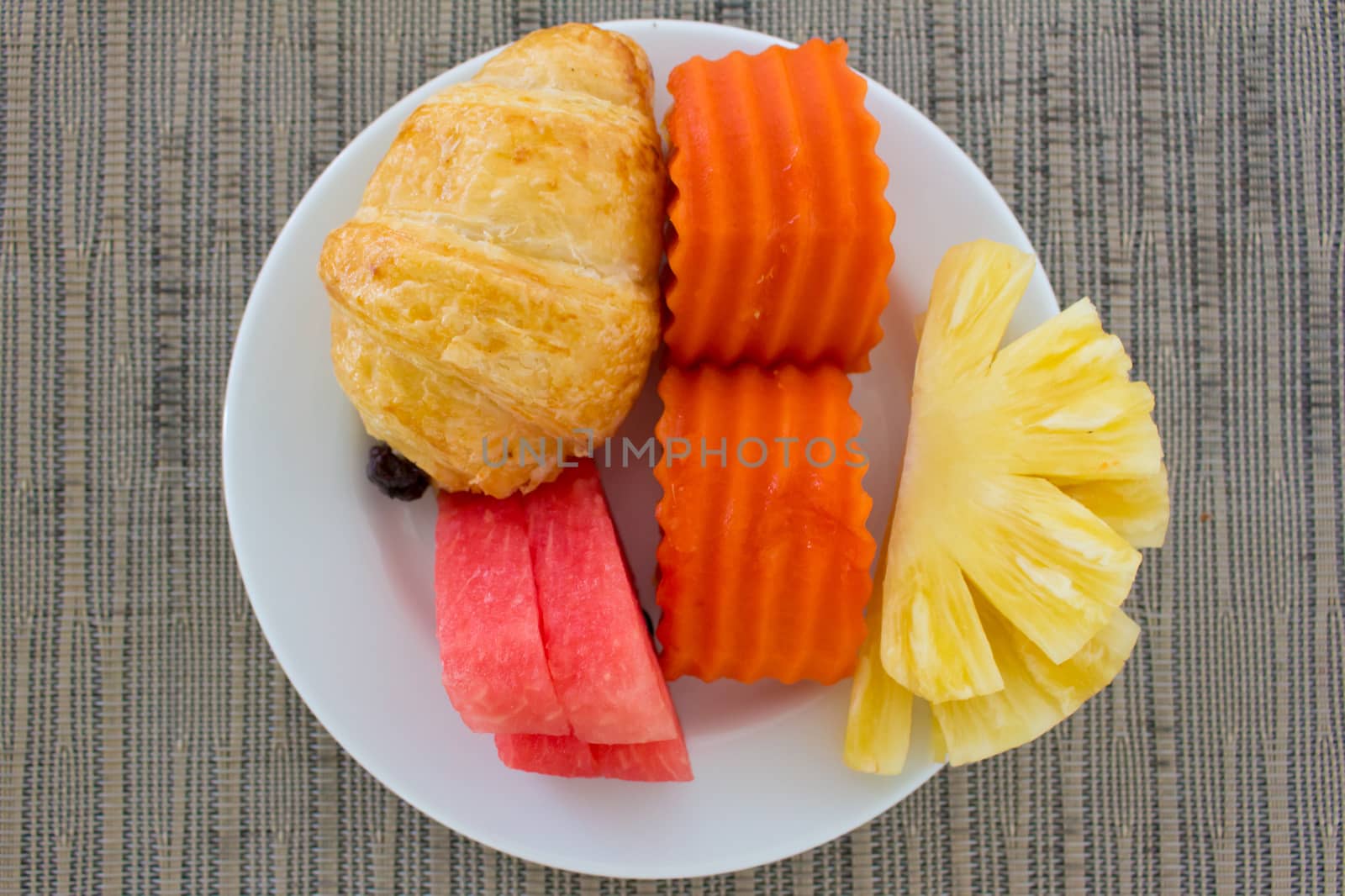 Breakfast with fruits and a piece of bread on the white plate, top view