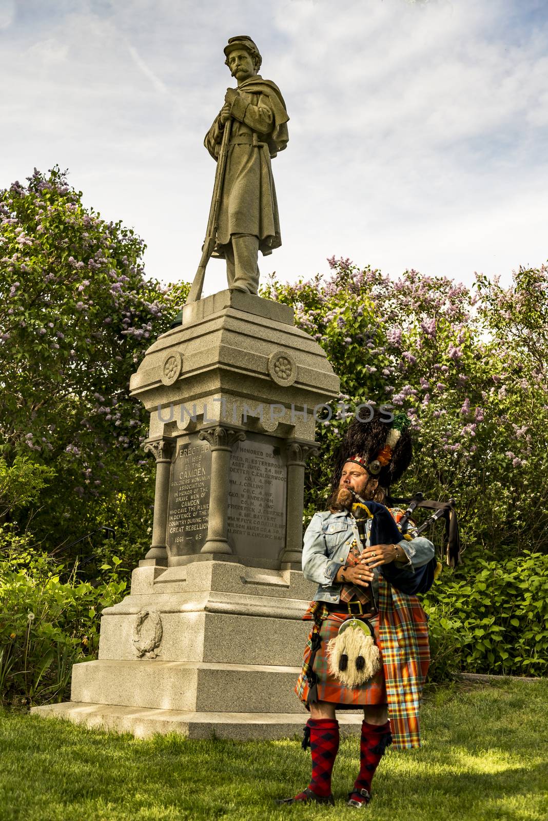 CAMDEN ME - MAY 28: Scottish bagpiper dressed in traditional red and black tartan dress under a American soldier statue on May 28, 2016 in Camden ME, USA