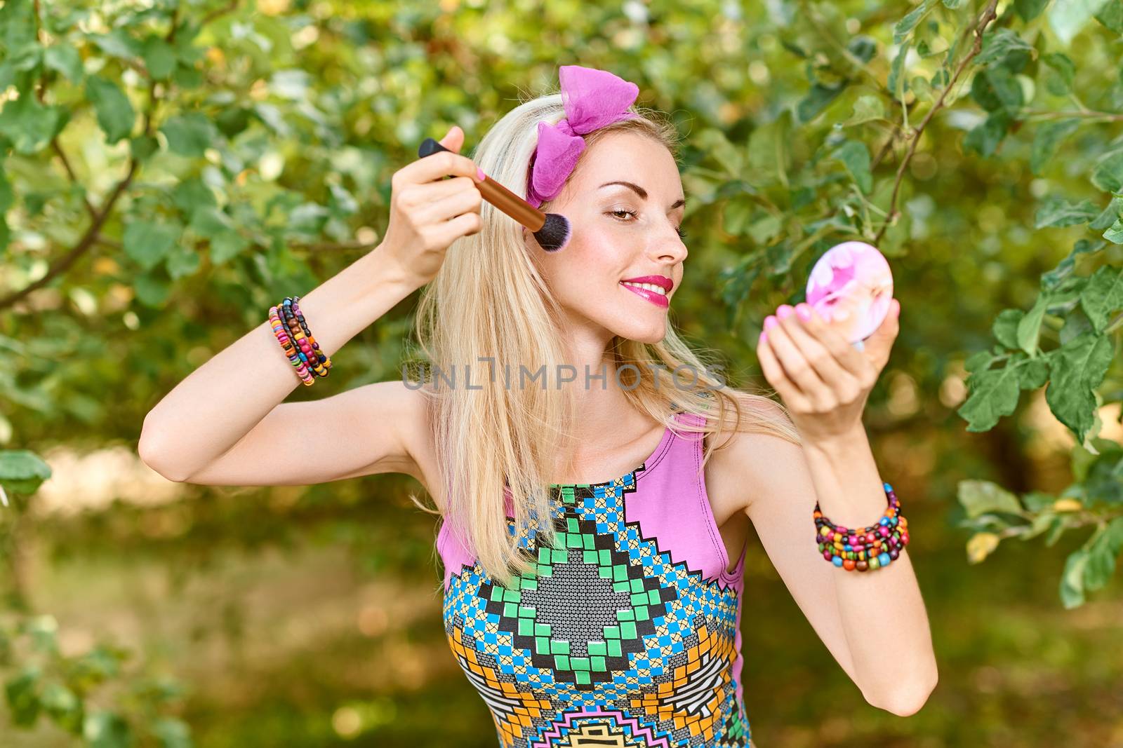 Beauty portrait stylish playful woman smiling primping with mirror, park, people, outdoors. Attractive hipster happy pretty blonde girl with bow, fashionable top. Relax, summer garden, lifestyle,bokeh