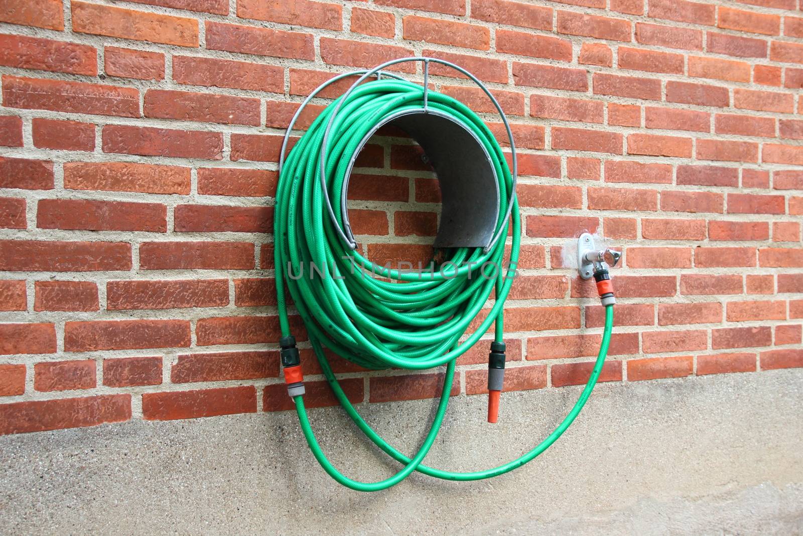 Green water hose hanging red brick wall