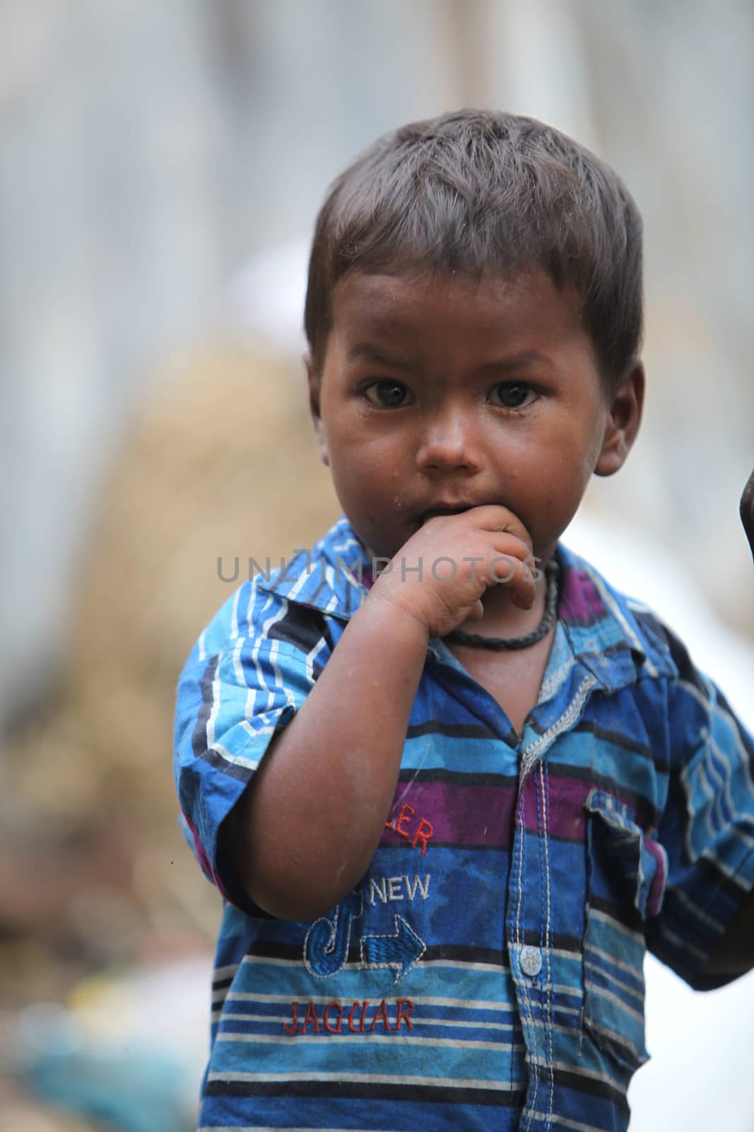 A portrait of a poor little Indian boy putting finger in his mouth.