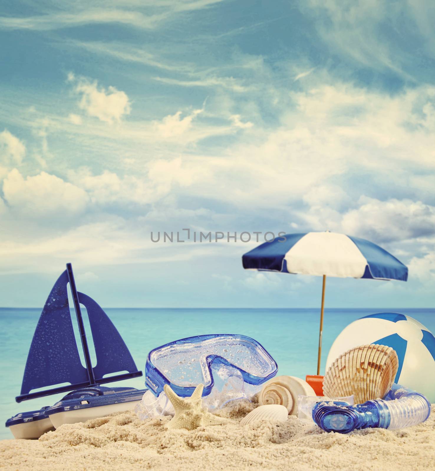 Beach toys on sandy beach with blue sea in background by Sandralise