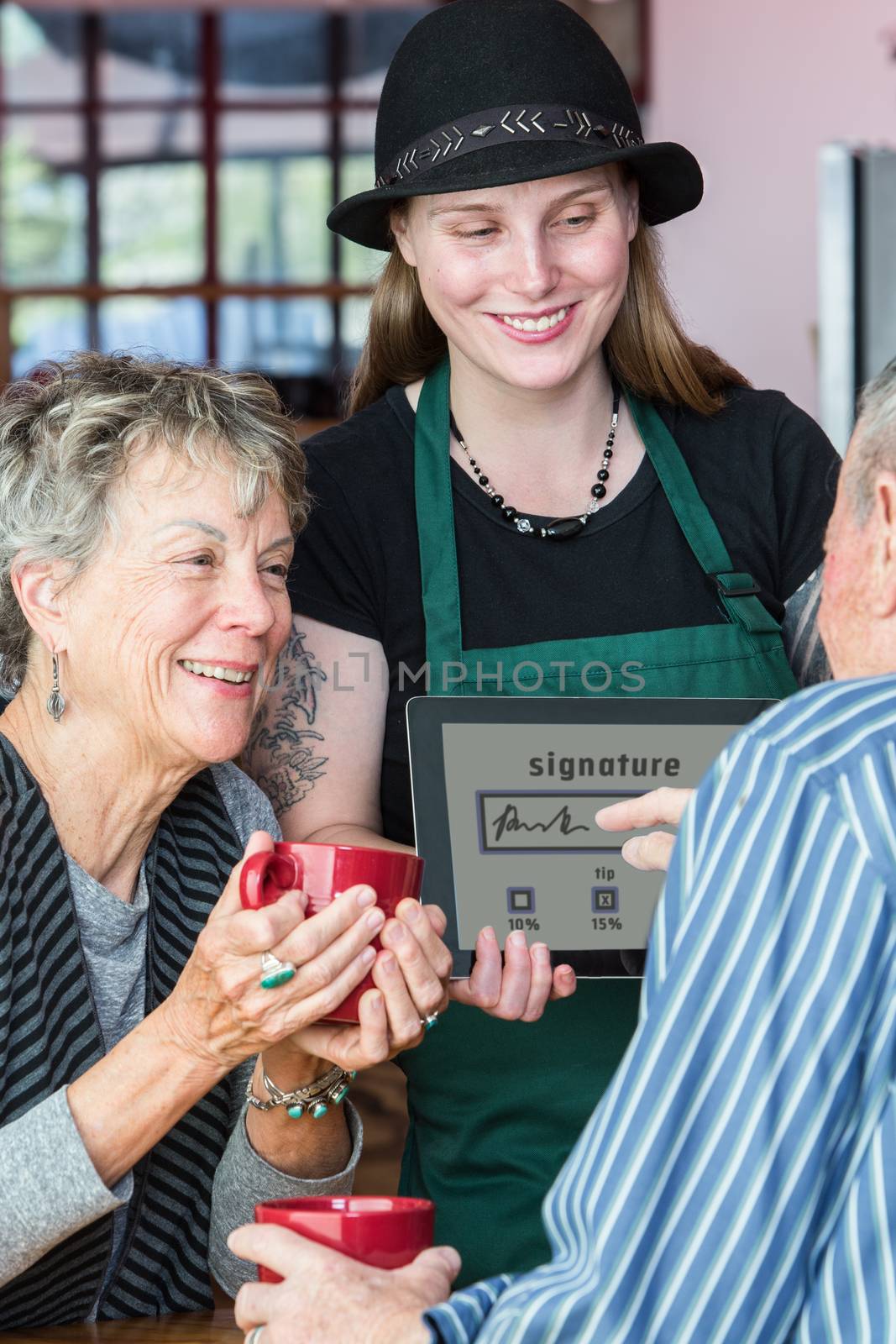 Senior signs name on a tablet to pay bill in coffee house