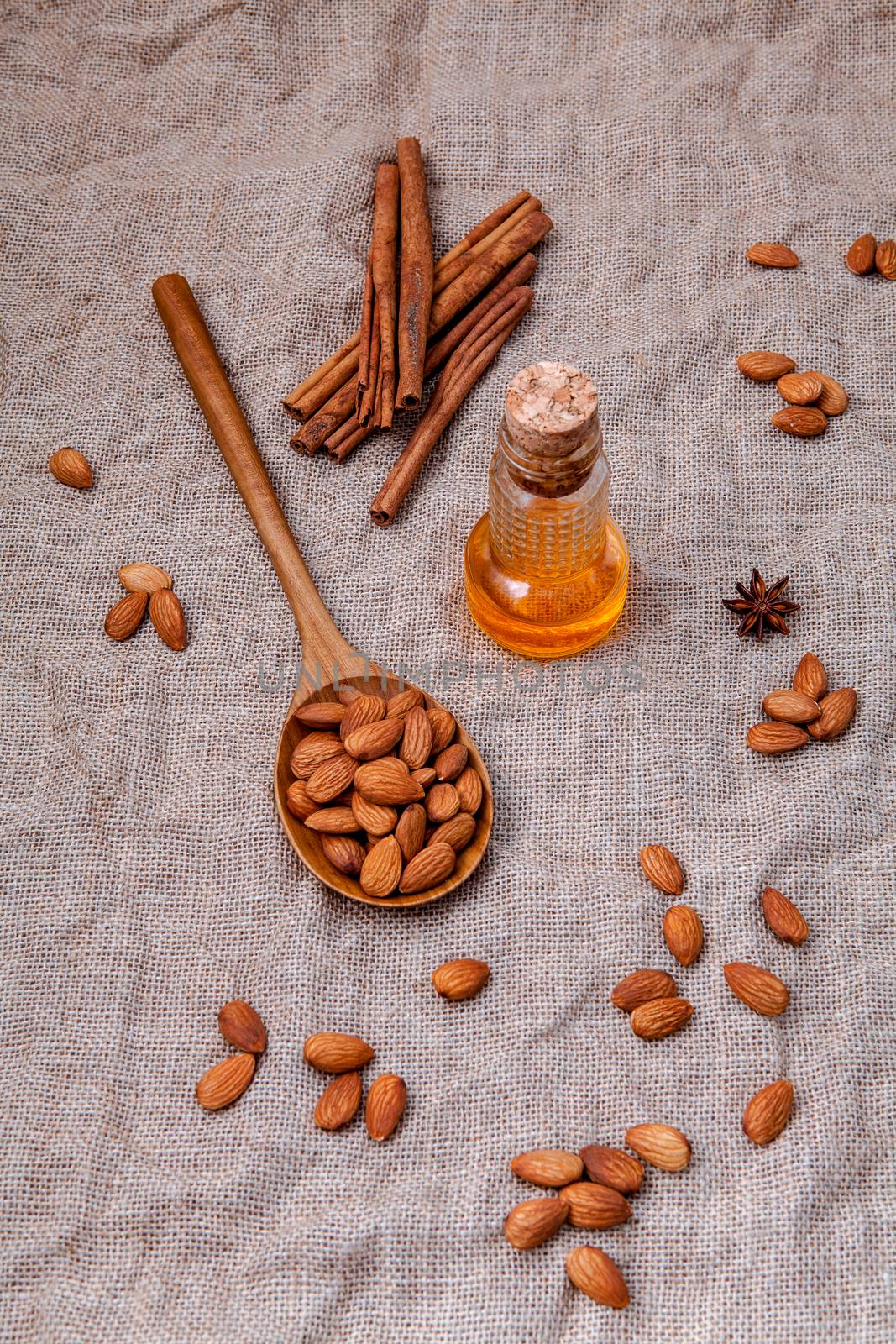 Bottle of extra virgin almonds oil with whole almonds and cinnamon sticks on hemp sack background.