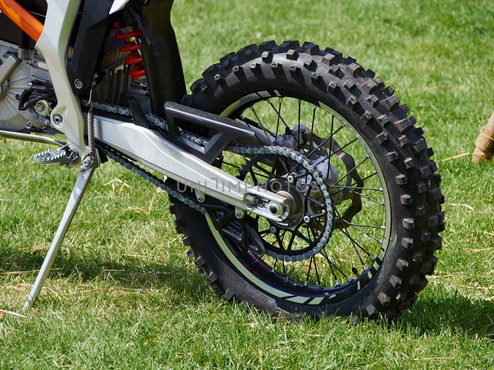 Close details of a rear wheel of a dirt motocross bike standing on the grass