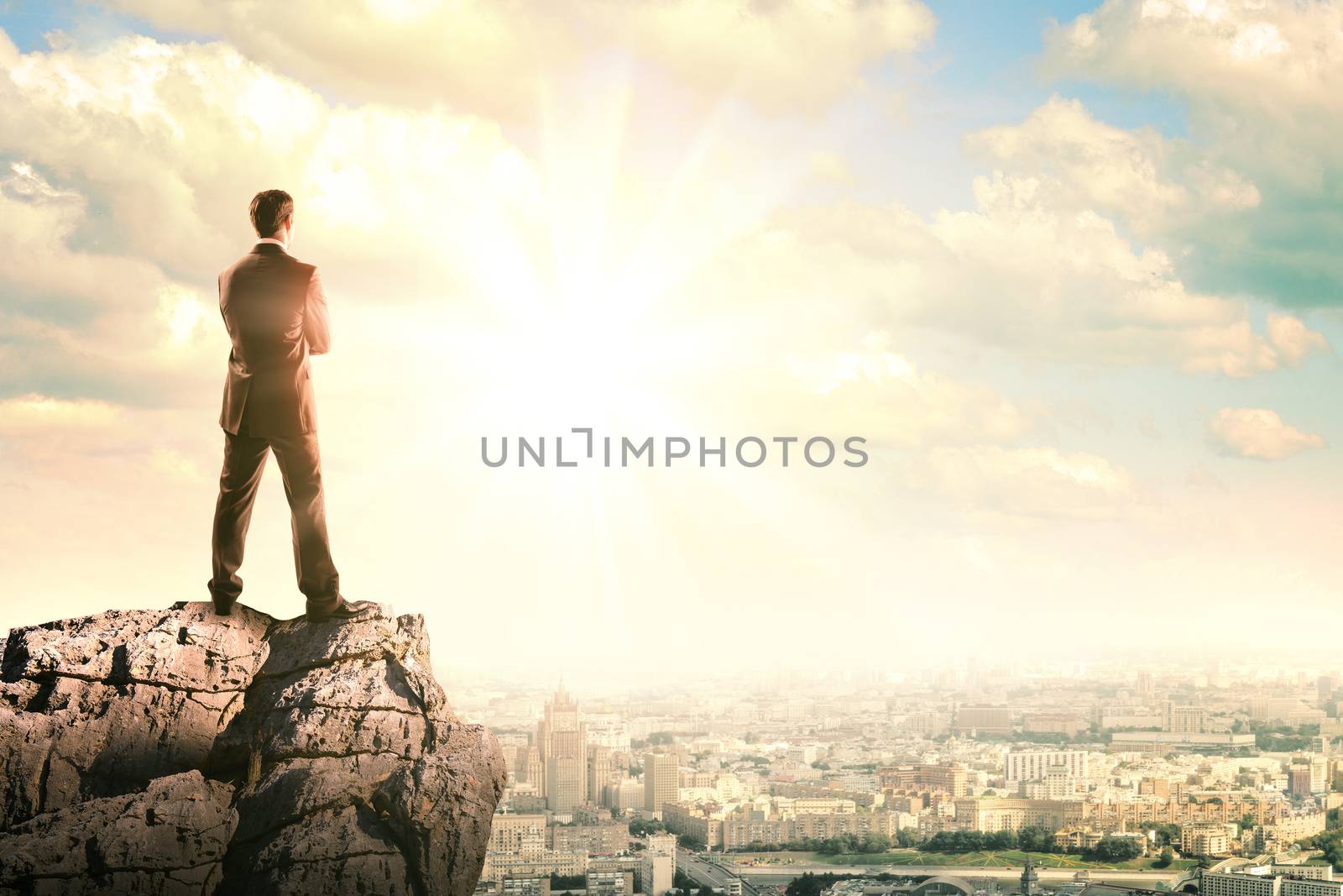Young businessman standing on edge of rock by cherezoff