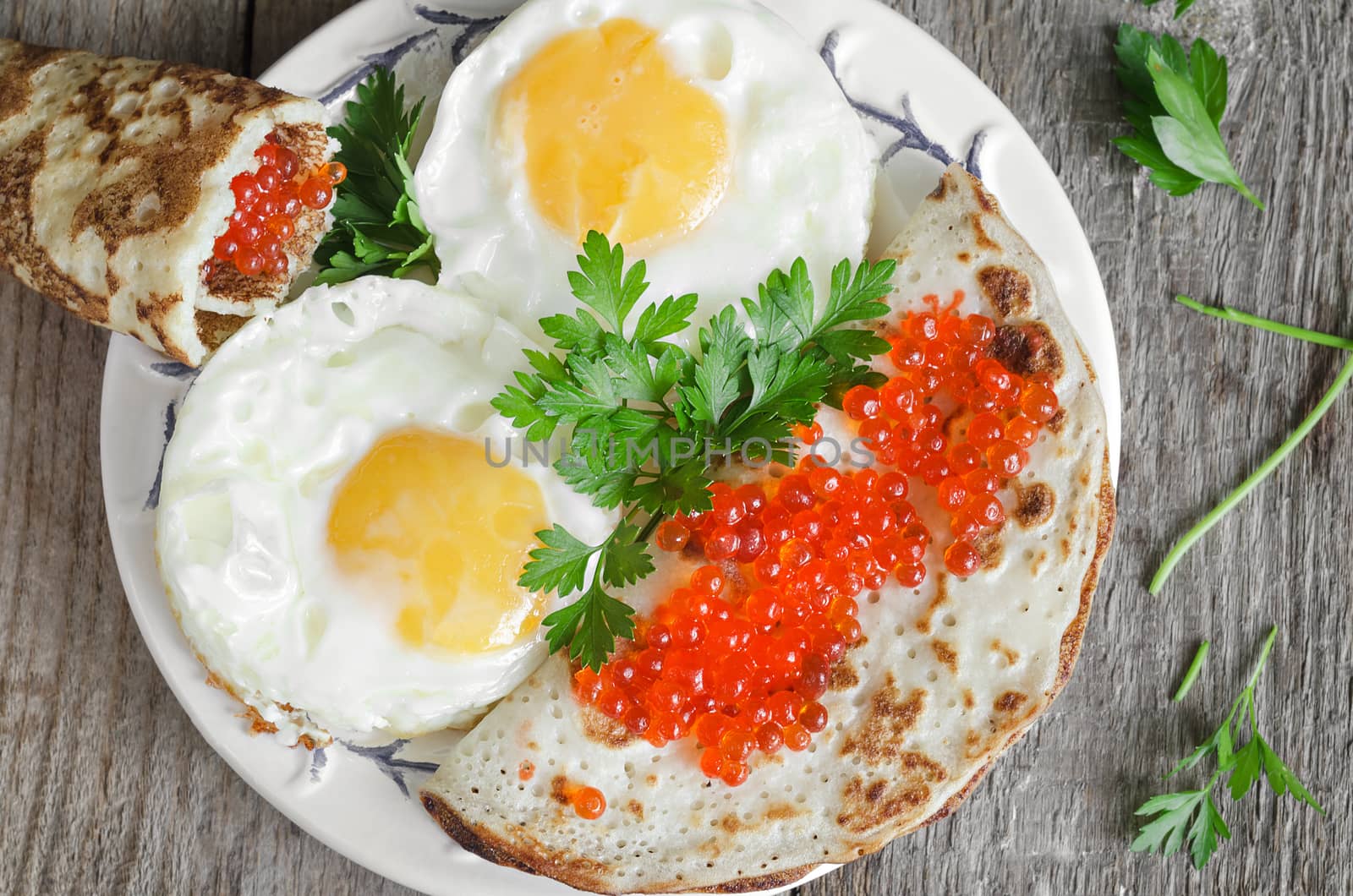 Scrambled eggs and pancakes with red caviar on an old wooden surface.
