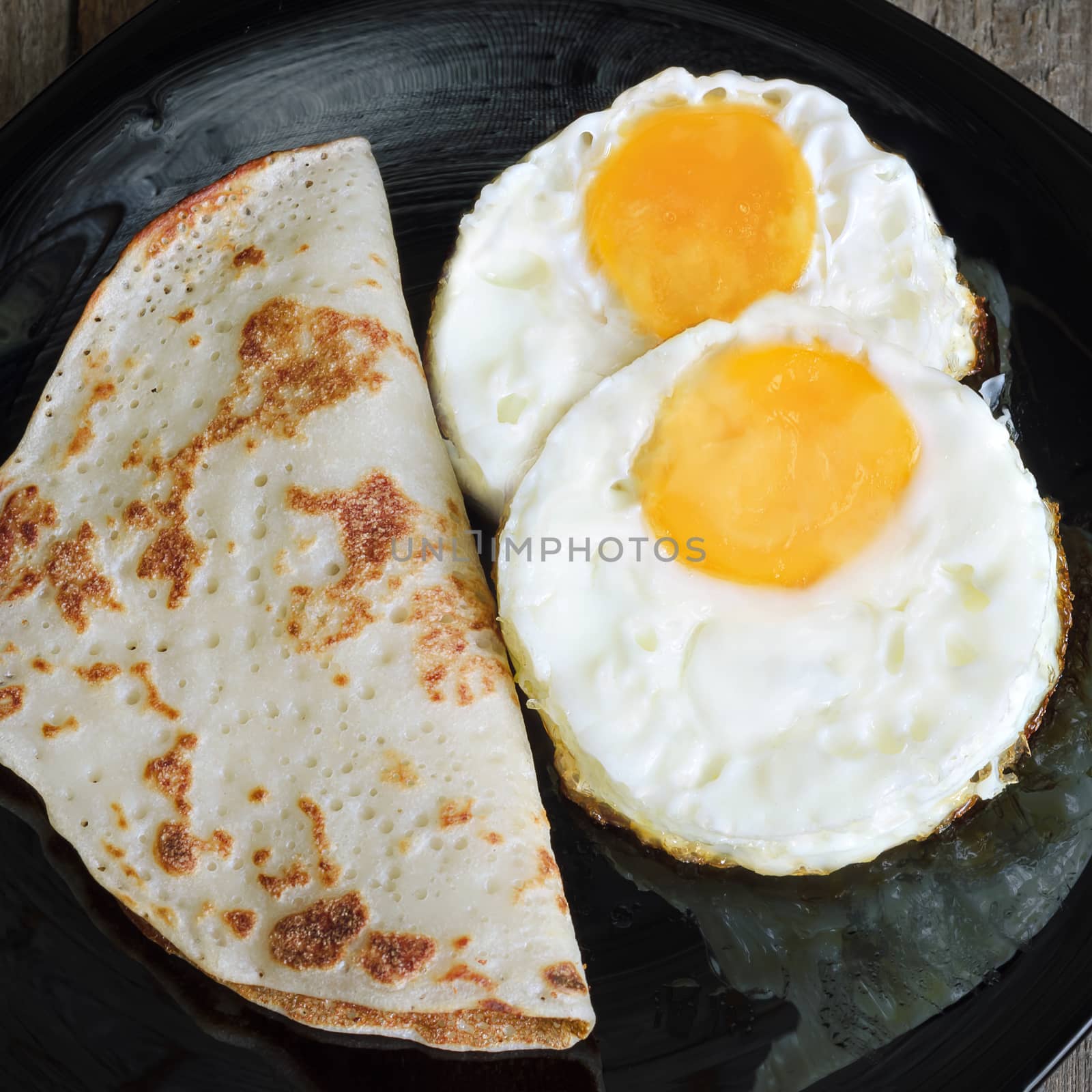 Two fried eggs and pancakes on a black glass plate, close-up