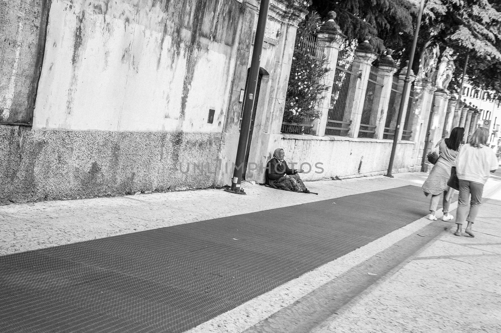 An old woman begging for coins to two woman passing by in the street.