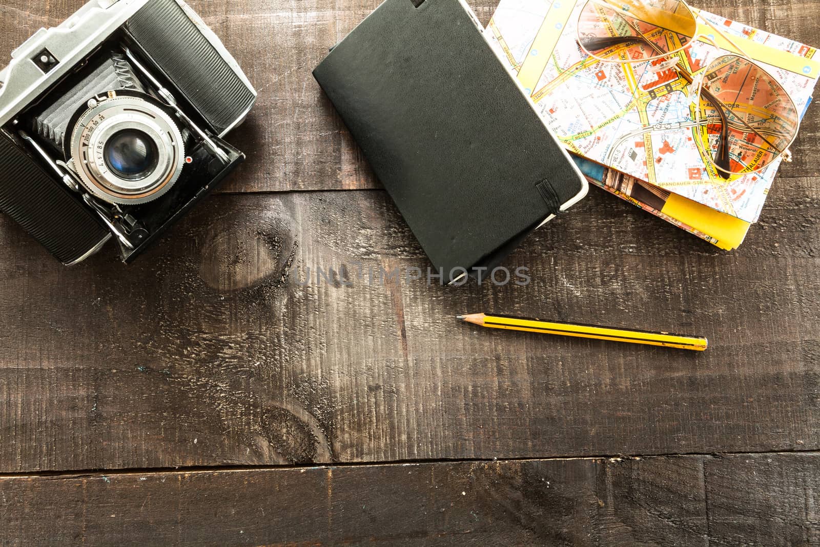 Vintage camera, a map, sunglasses case, polaroid paper an a pencil  on a light wood table