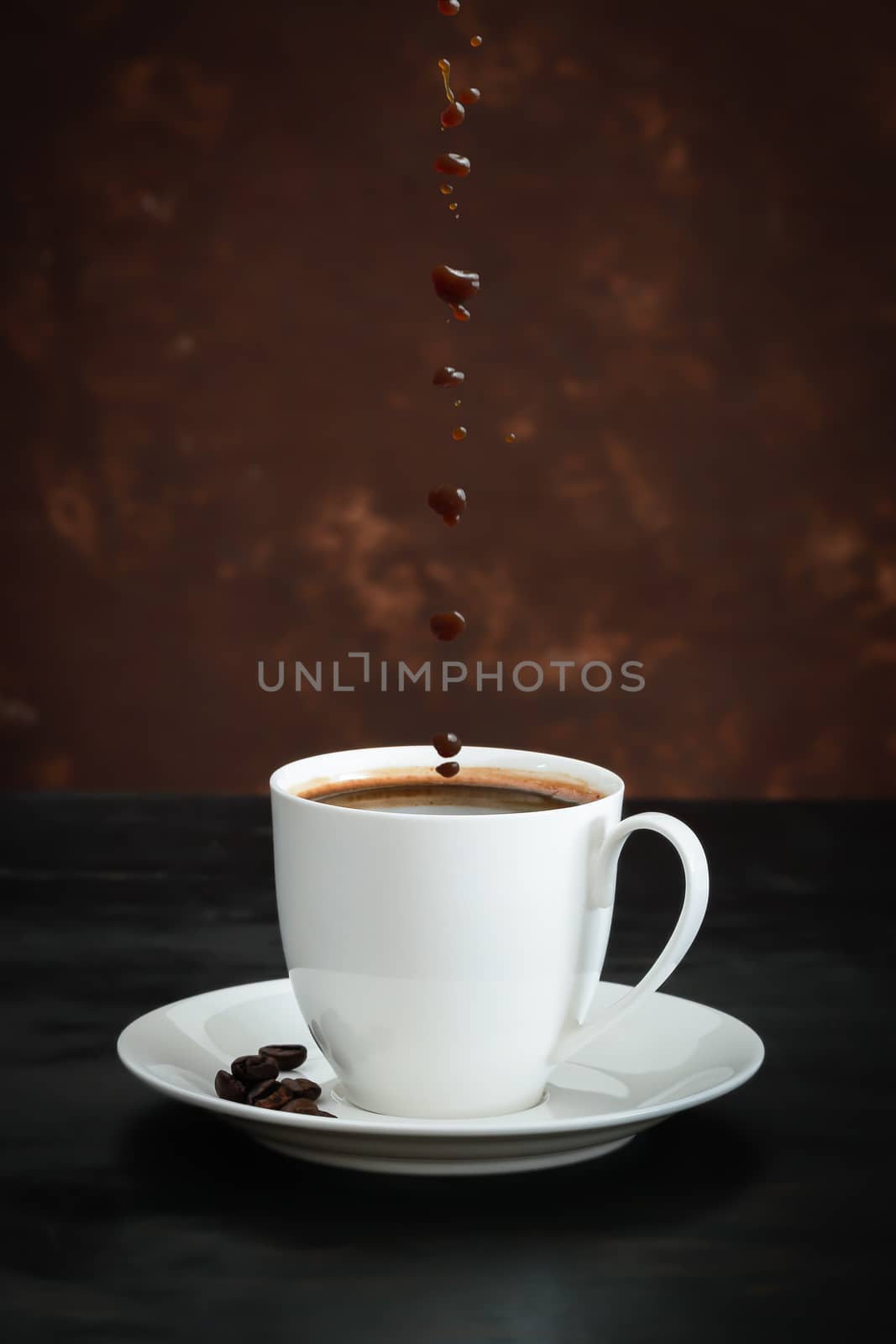 Coffee cup and beans with coffee drops on black wood background.