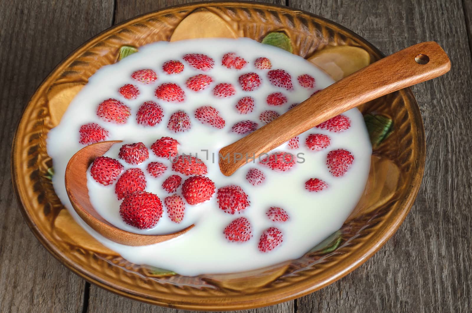 Strawberry with milk in a ceramic bowl and spoon on old wooden background